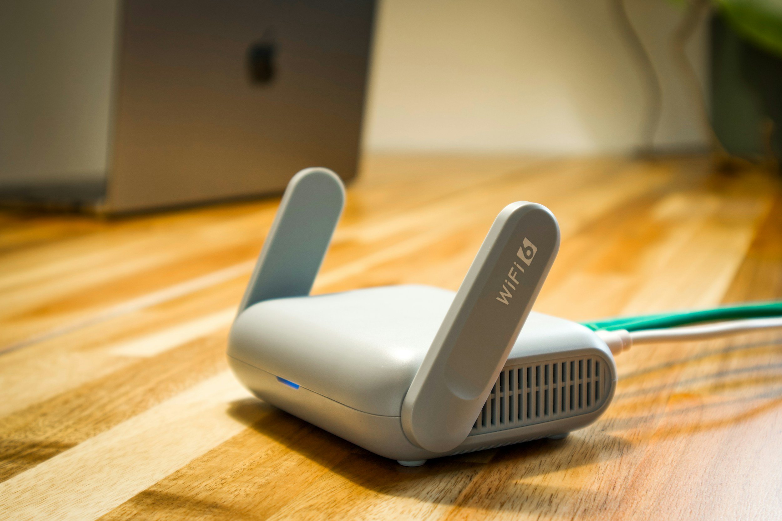 A white WiFi router with two antennas sitting on a wooden surface.