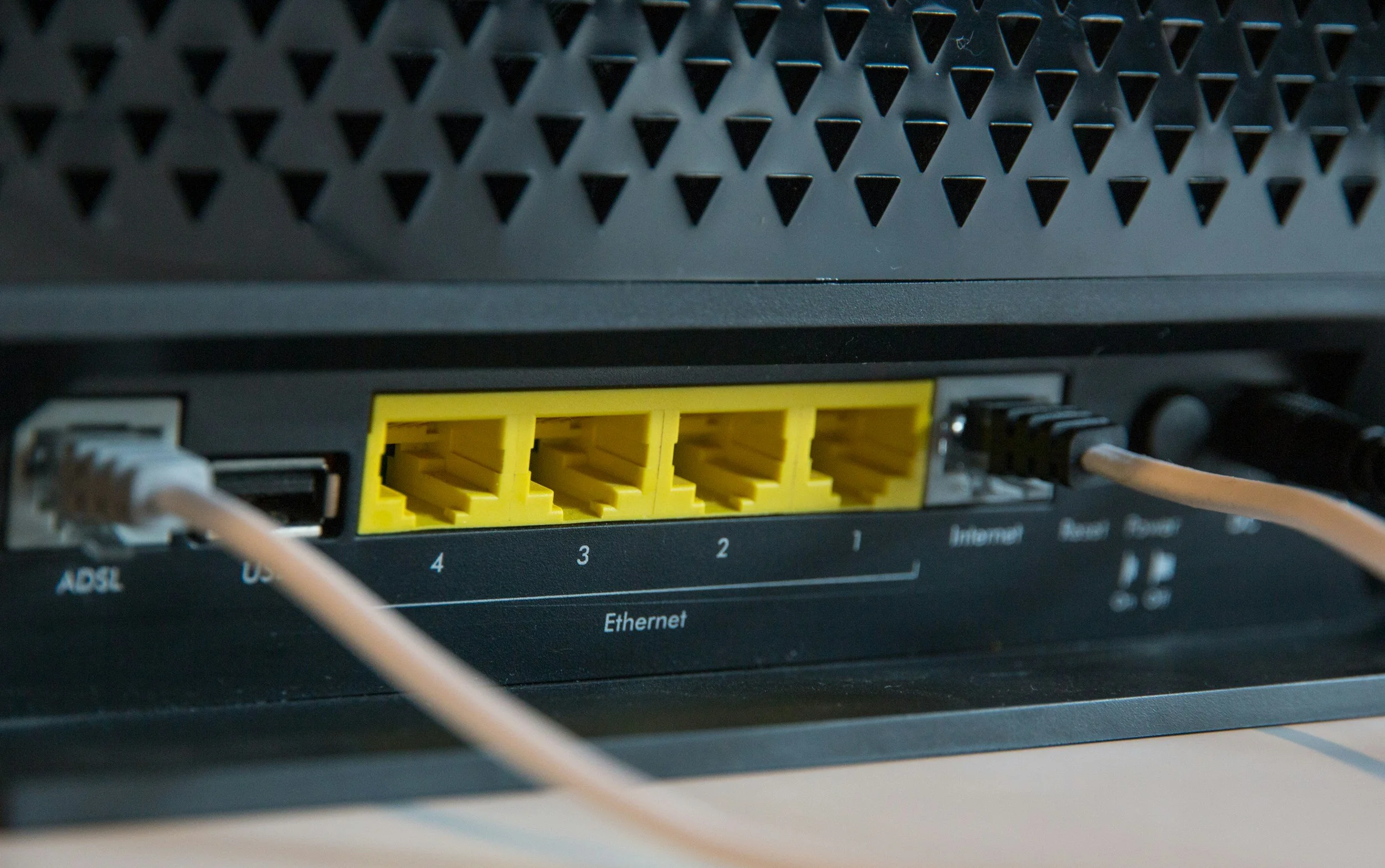 Close-up of a computer network router with yellow Ethernet ports and a white Ethernet cable plugged into one of the ports.