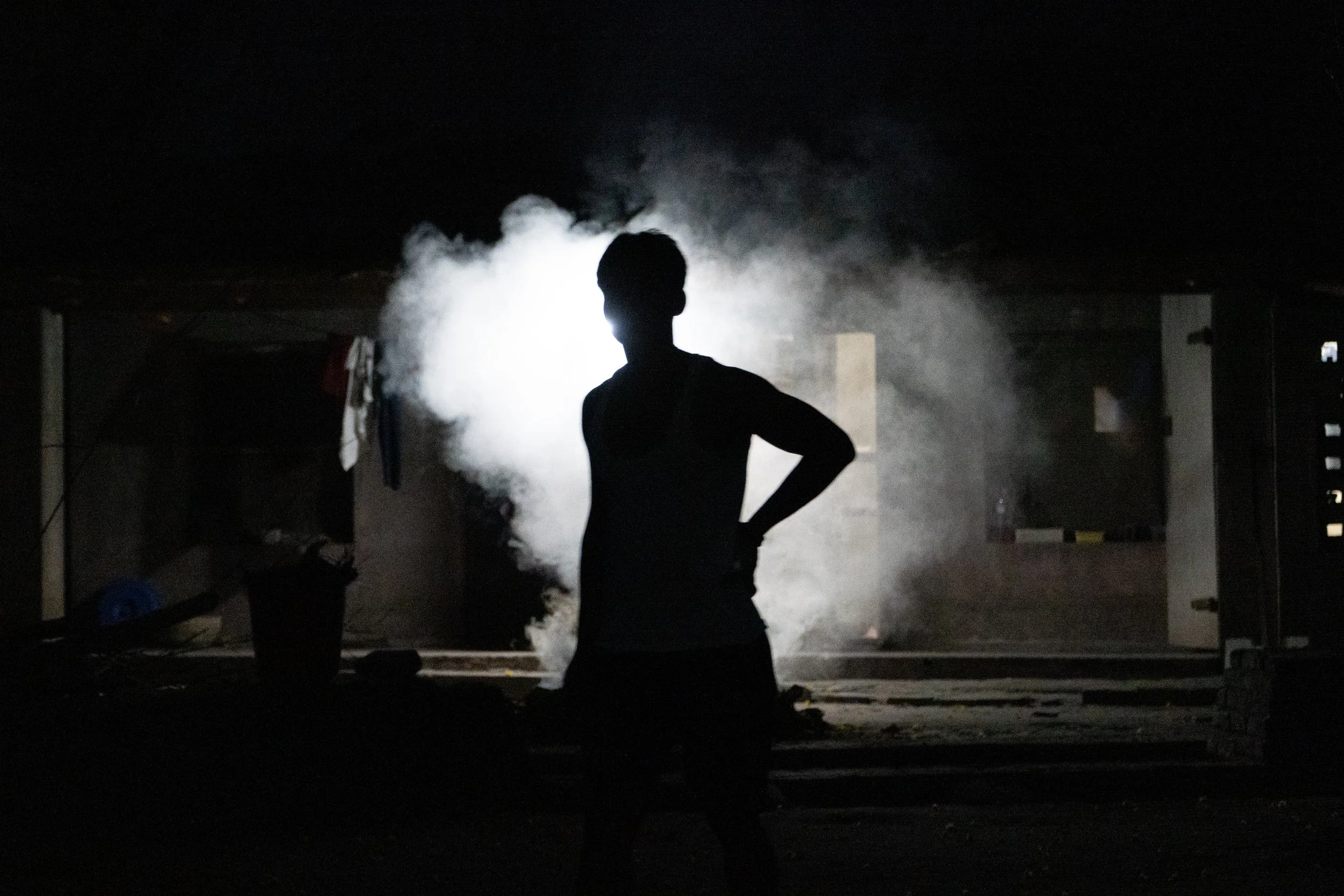 Silhouette of a person standing in a dark room with smoke or vapor backlit by bright light.