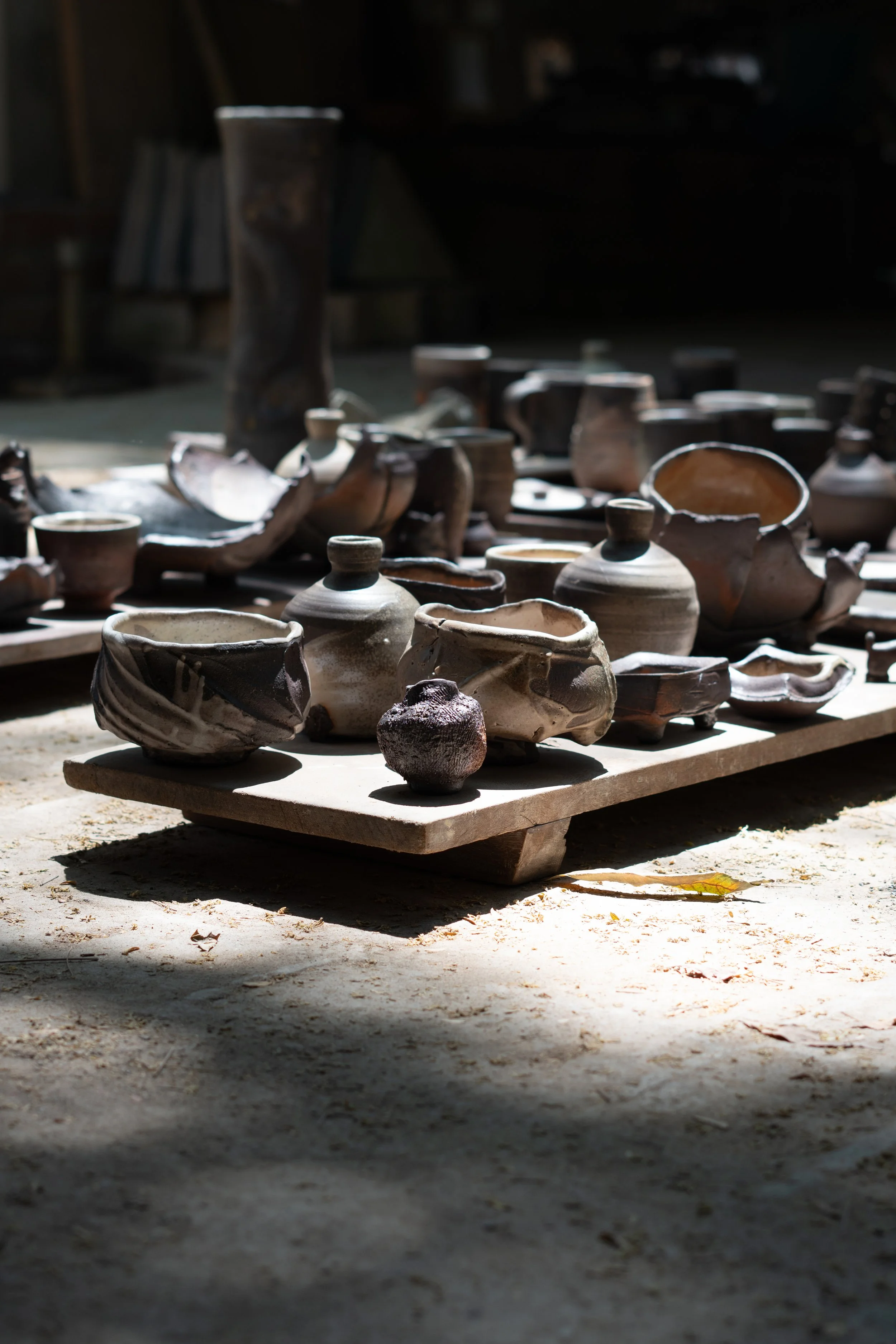 Clay pottery pieces displayed on a wooden platform outdoors with sunlight and shadows.