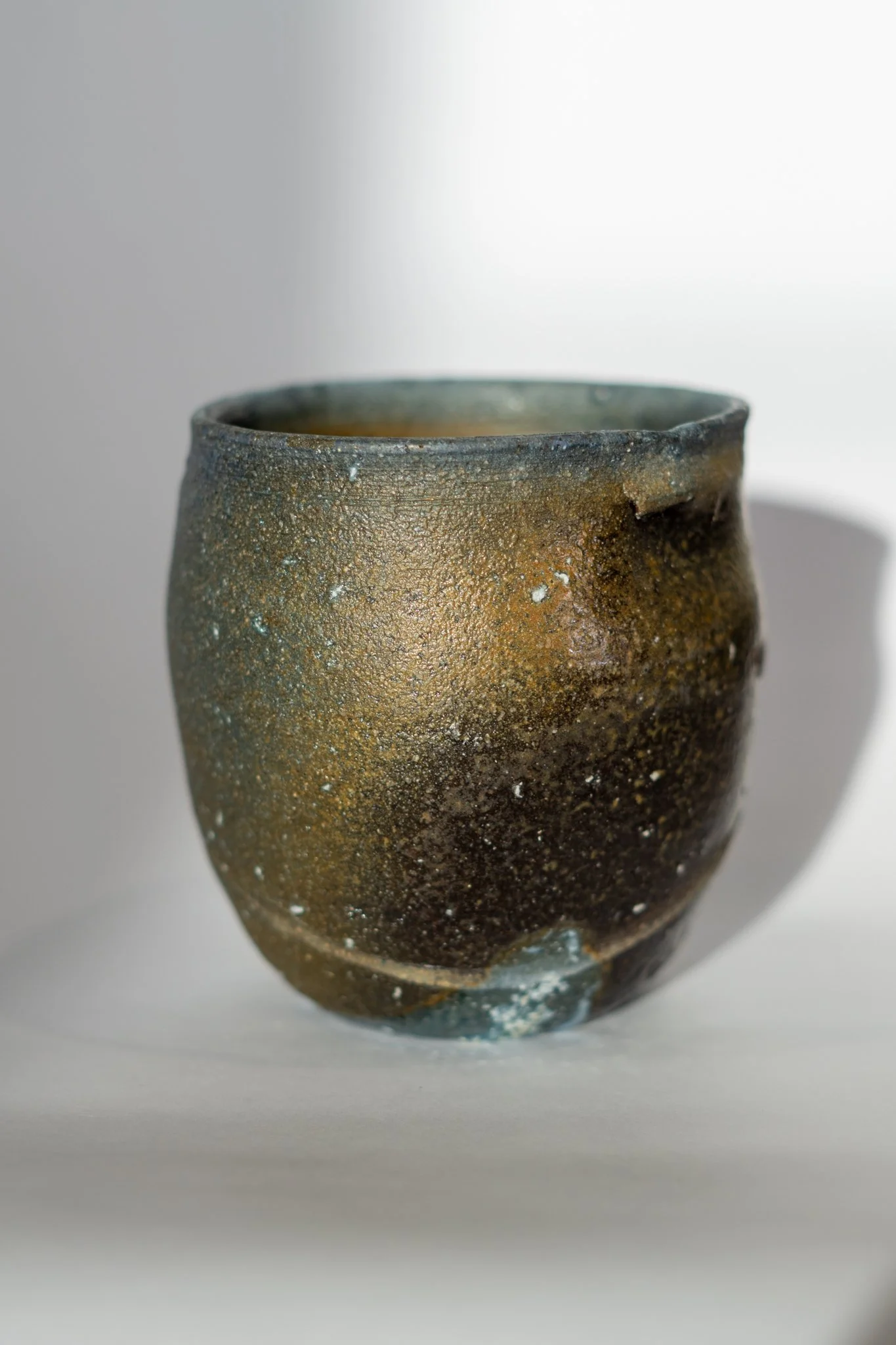Close-up of a rustic, textured ceramic vase with a narrow opening and uneven surface, set against a plain white background.