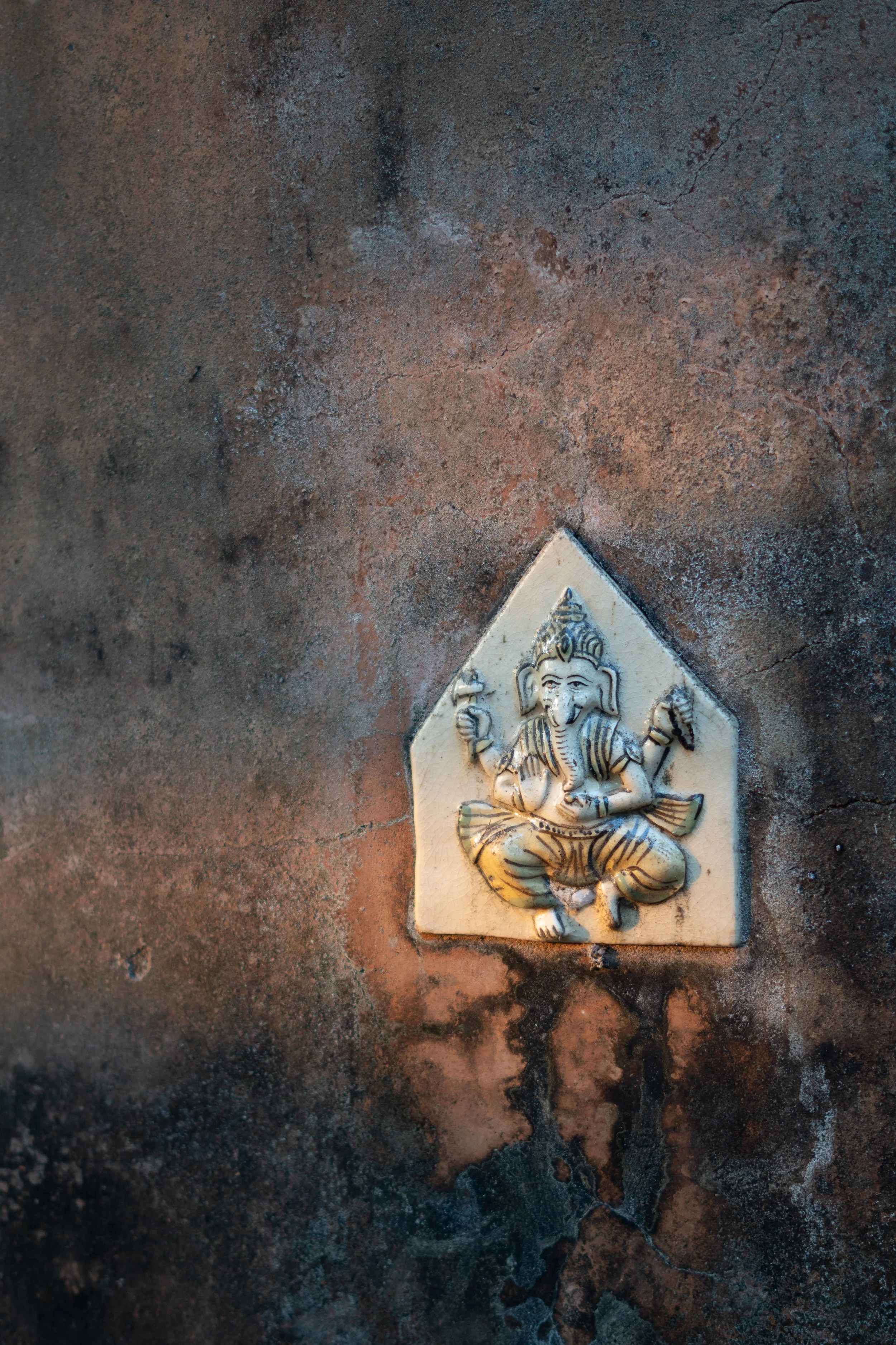 A decorative ceramic tile featuring Lord Ganesha, a Hindu deity, lying on a surface with a textured, earthy background.