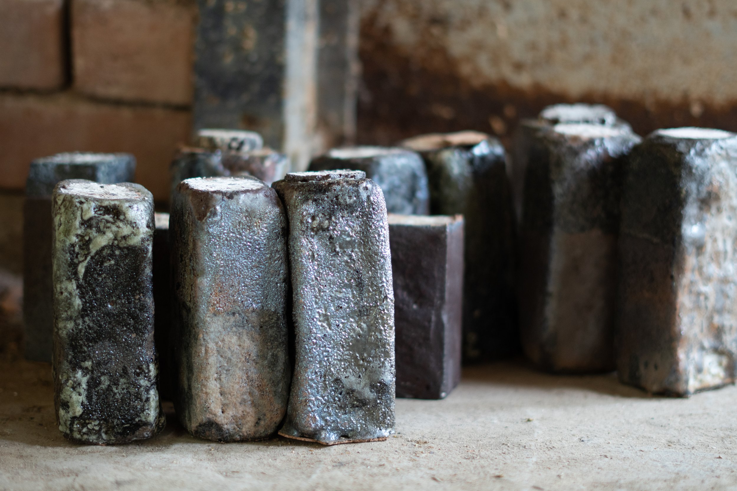 A row of weathered metallic nails or tools with rust and dirt on a concrete surface against a brick wall background.