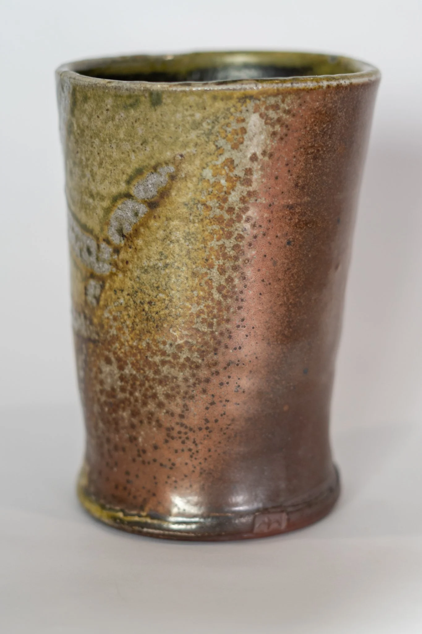 A ceramic mug with a gradient glaze from greenish at the top to reddish-brown at the bottom, featuring textured and speckled surface details.