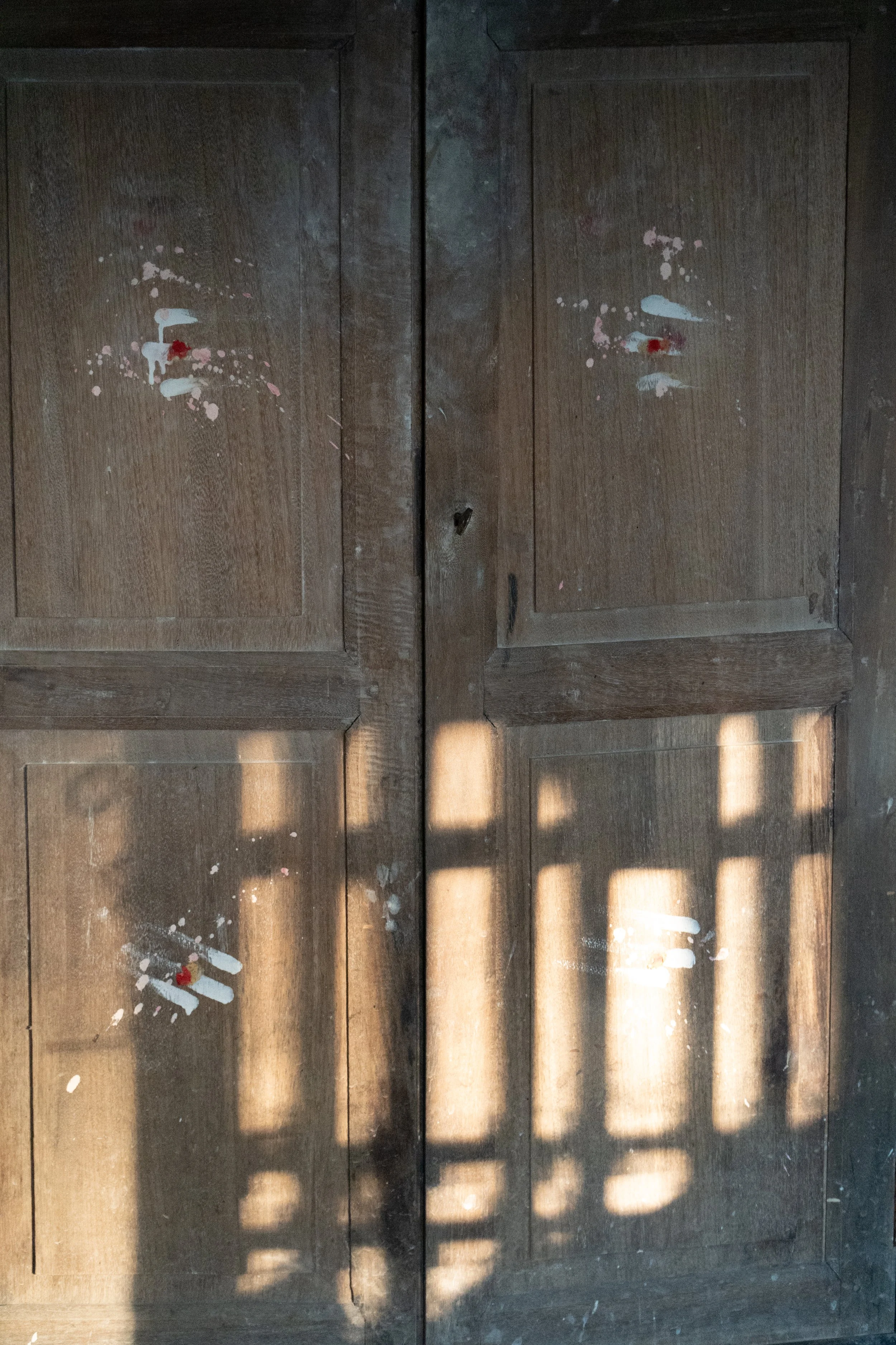 Paint splatters and handprints on wooden cabinet doors with sunlight casting shadows.