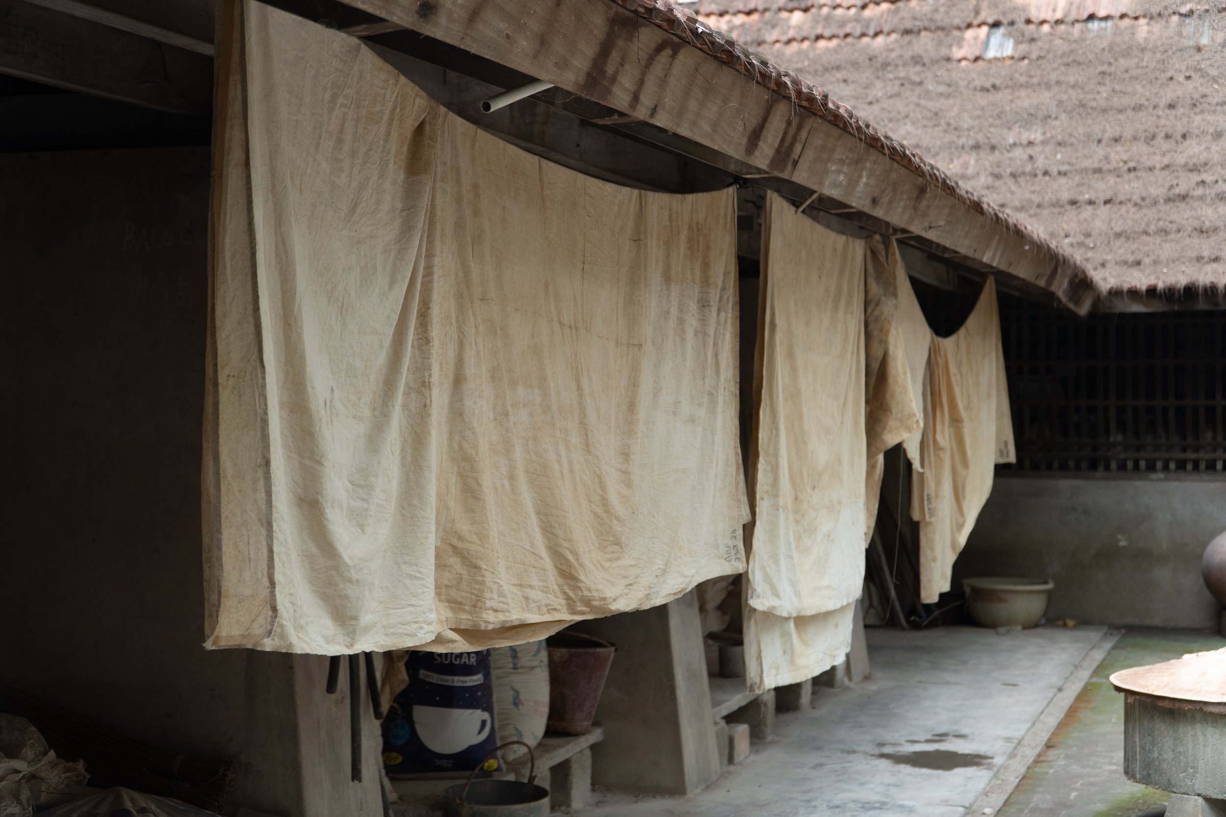 Clothes hang to dry outside on a clothesline under a tiled roof, with a rural setting visible in the background.