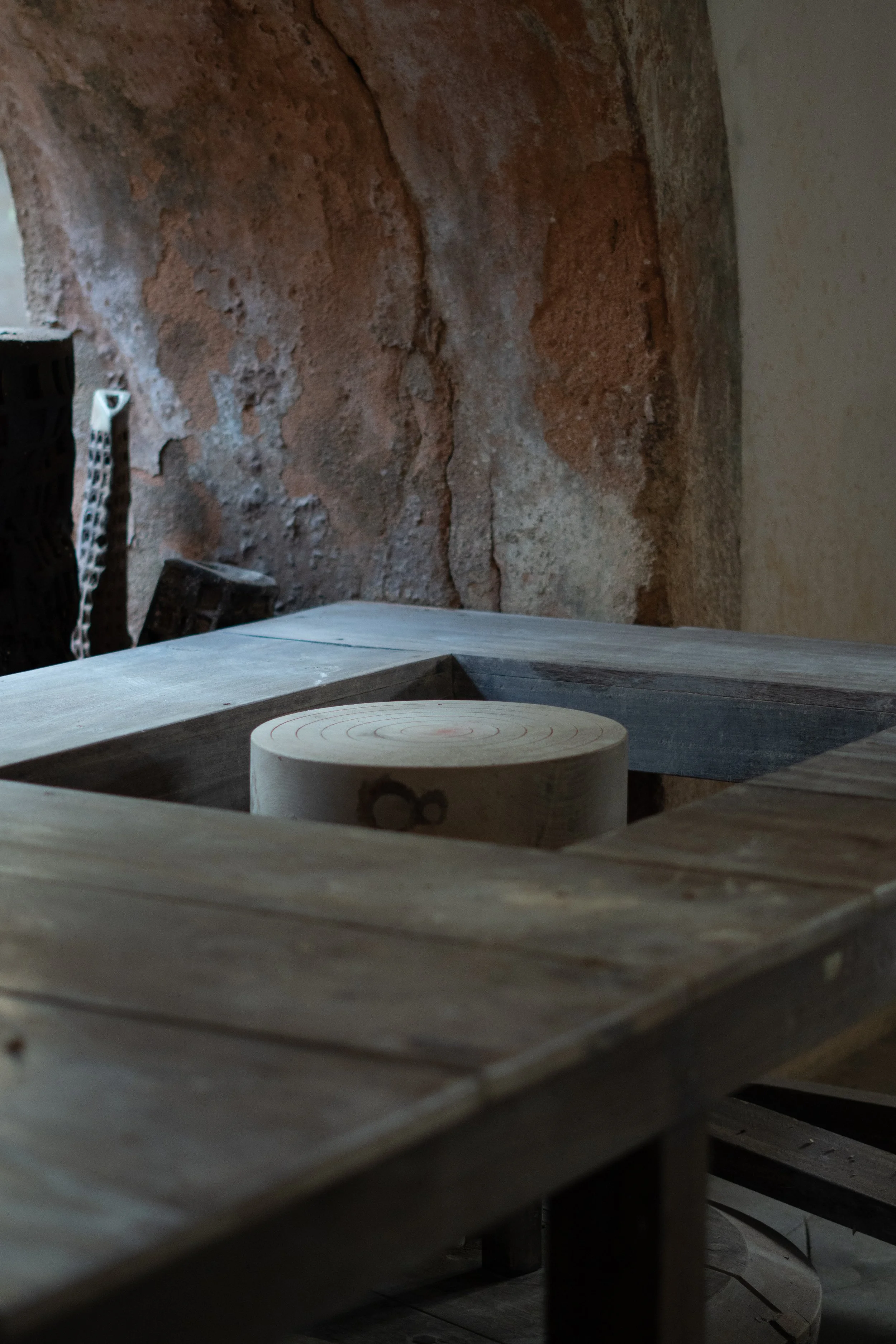 Close-up of a woodworking workspace with a wooden board, a circular saw blade, and some bricks in the background.