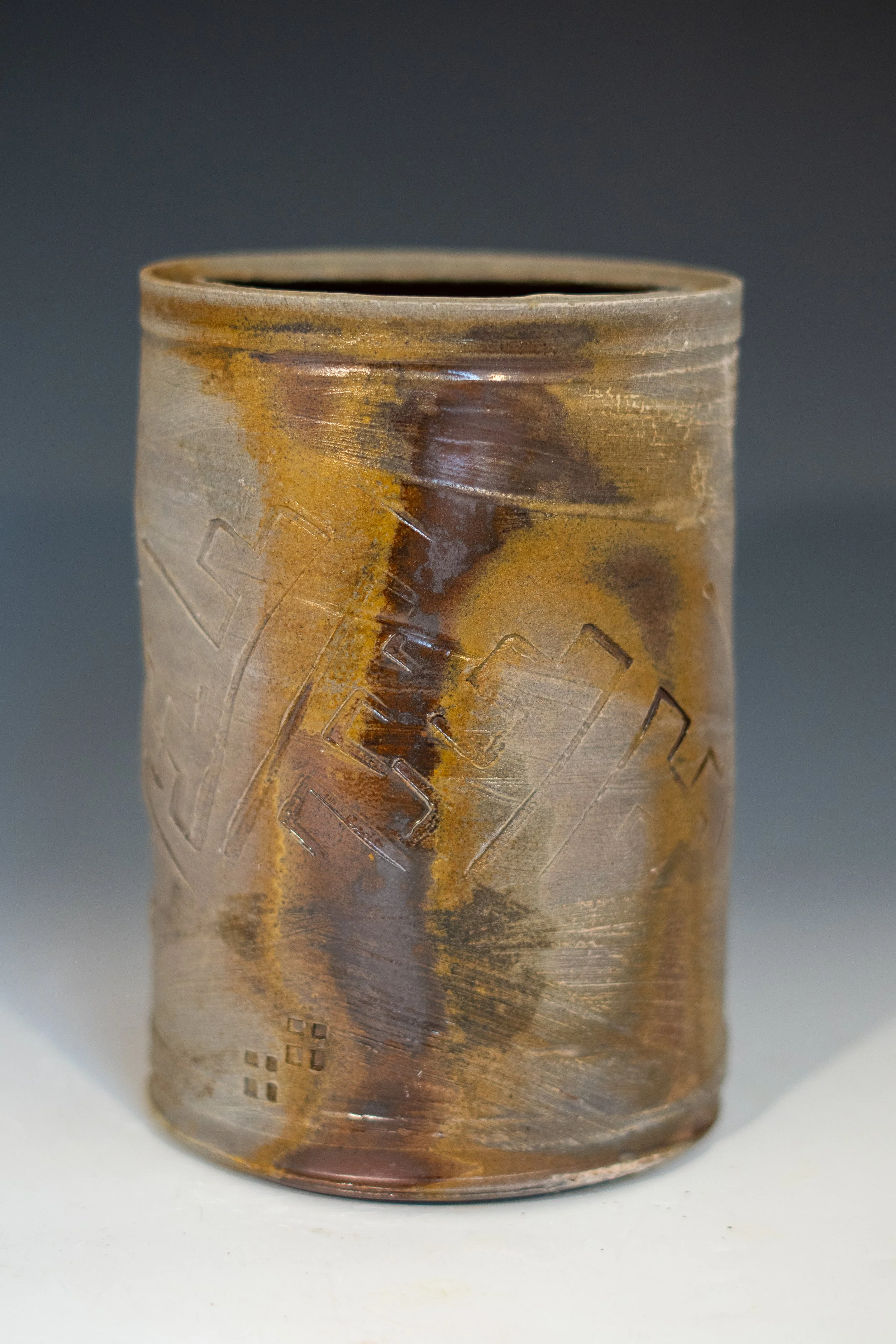 Close-up of a ceramic vessel with geometric and textured patterns, glazed in earthy tones of brown, yellow, and orange.