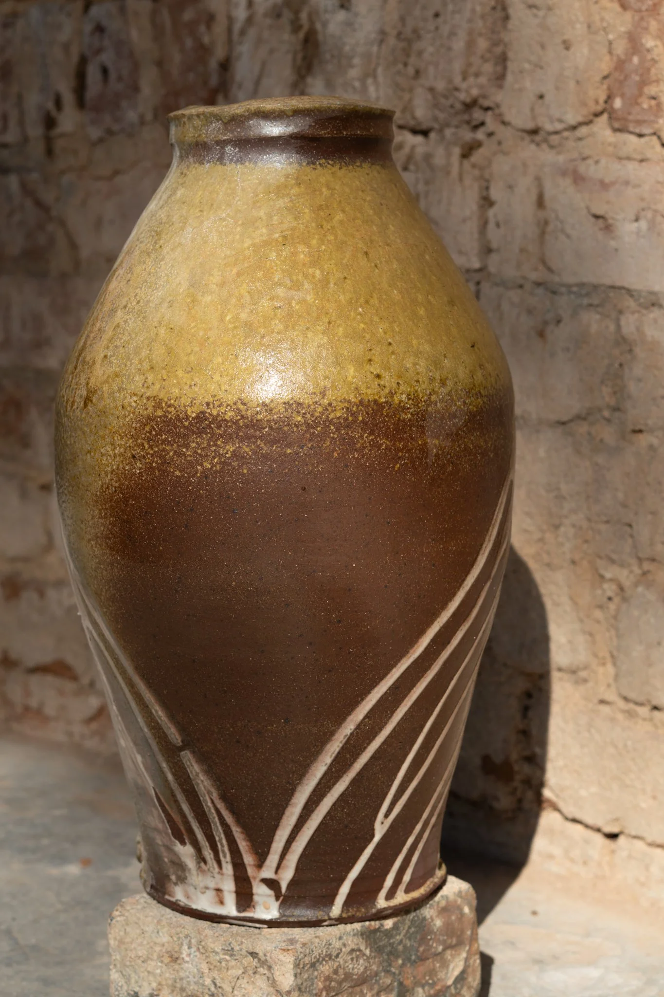 Close-up of a handmade ceramic vase with earthy glaze tones, featuring a striped design, set against a rustic brick wall background.