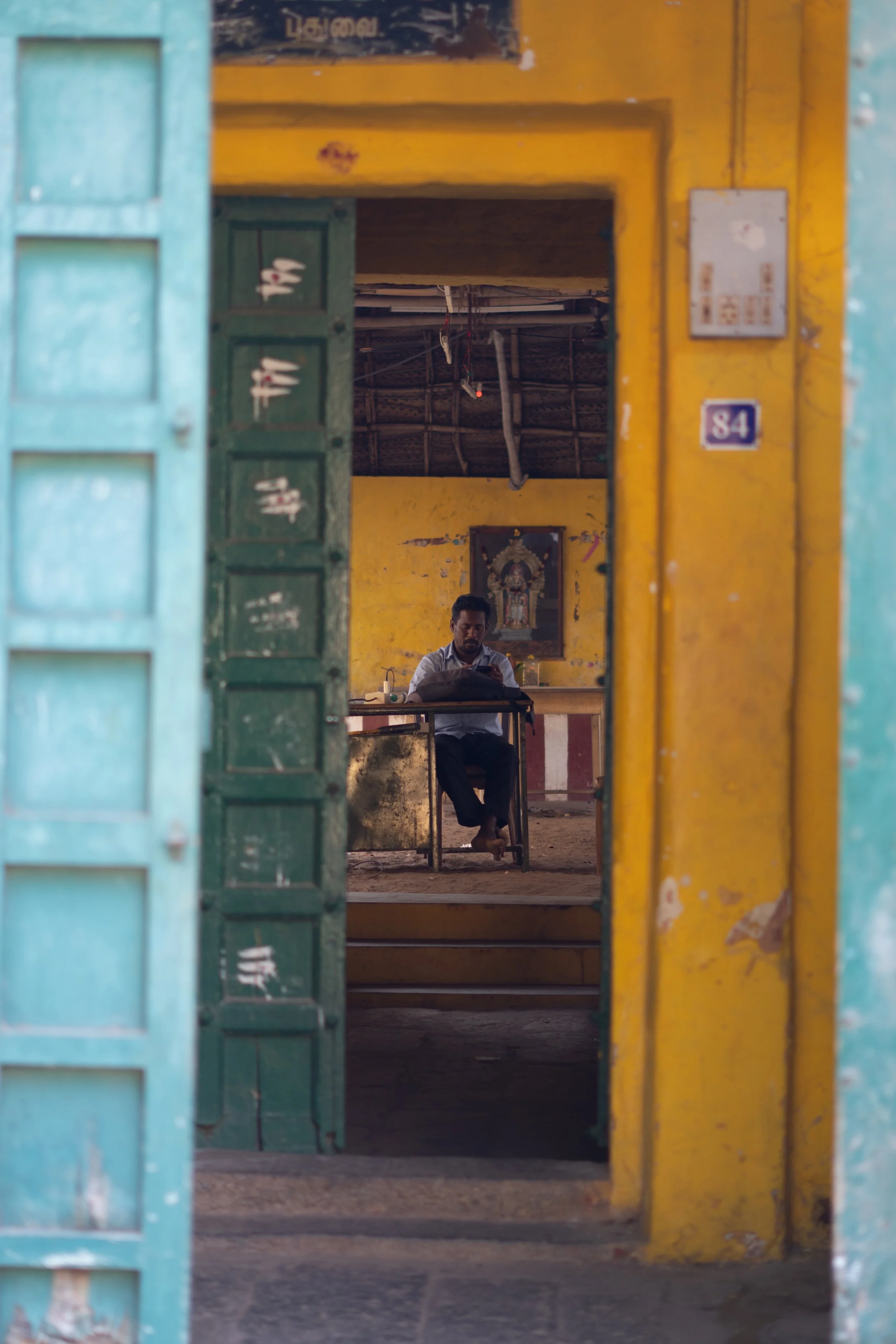 A man sitting at a desk inside a yellow-walled room, viewed through a doorway with blue, green, and yellow frames.