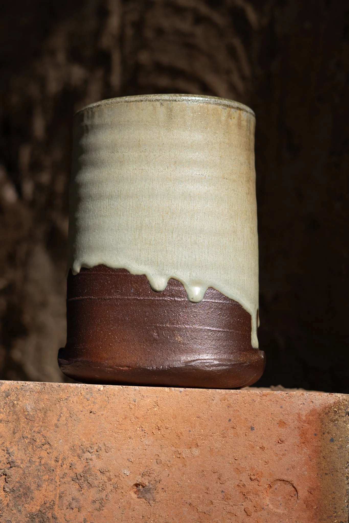 Close-up of a ceramic vase with a gradient glaze, transitioning from beige to brown, set against a dark, textured background.