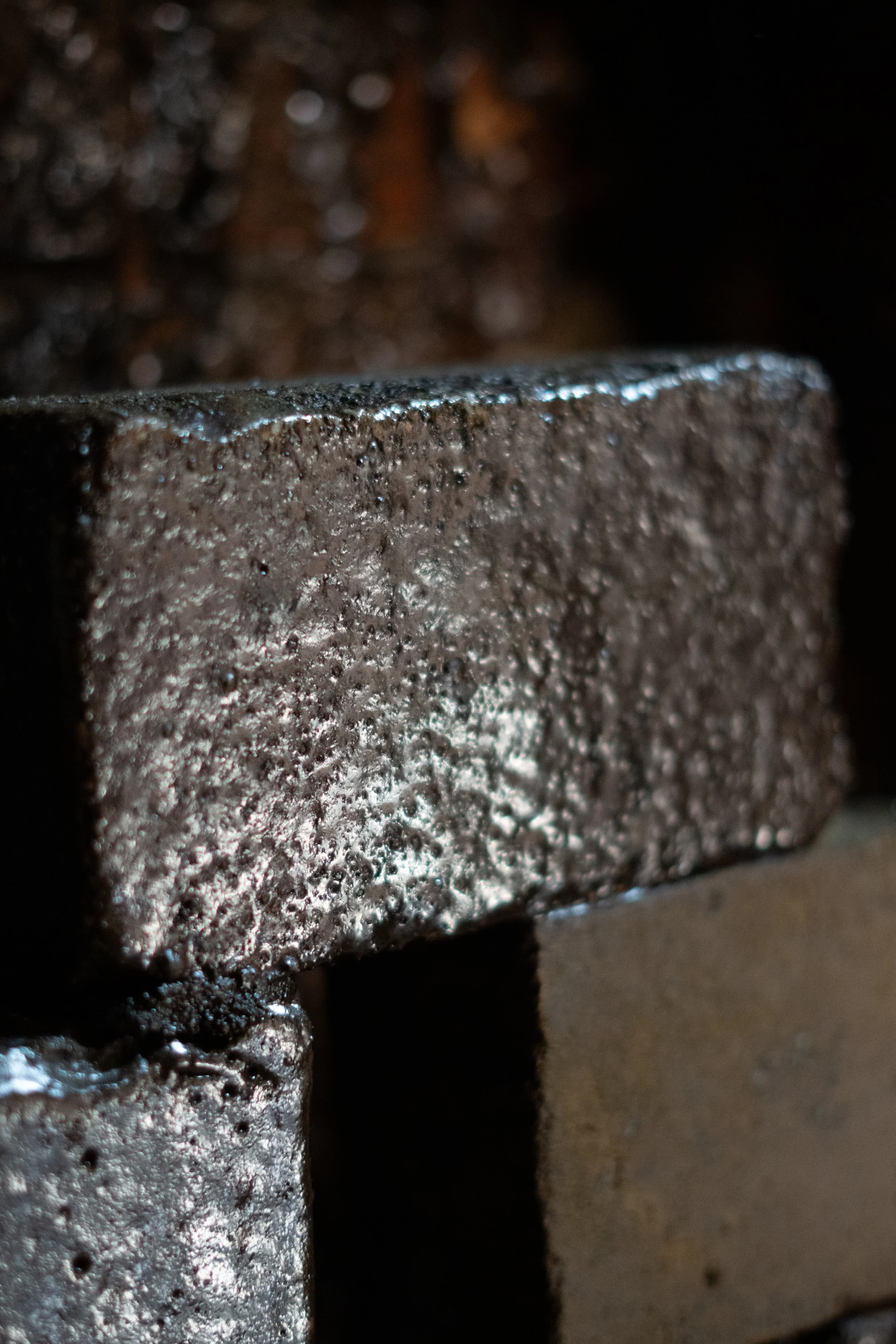 Close-up of a metallic surface, possibly a machine or industrial object, with a rough texture and shiny spots, in low light.