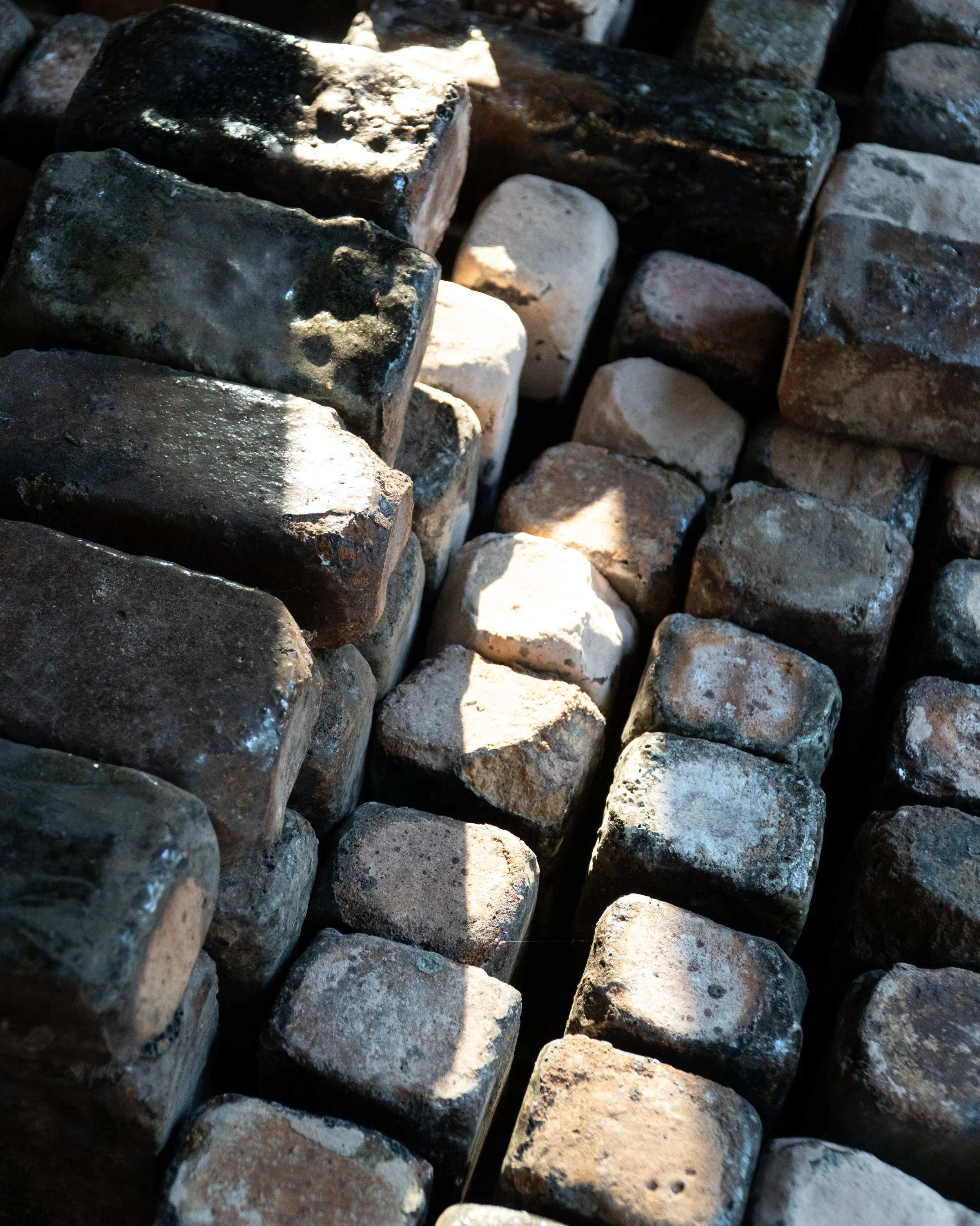 Close-up of stacked weathered stones or bricks with shadows and sunlight highlighting their rough textures.