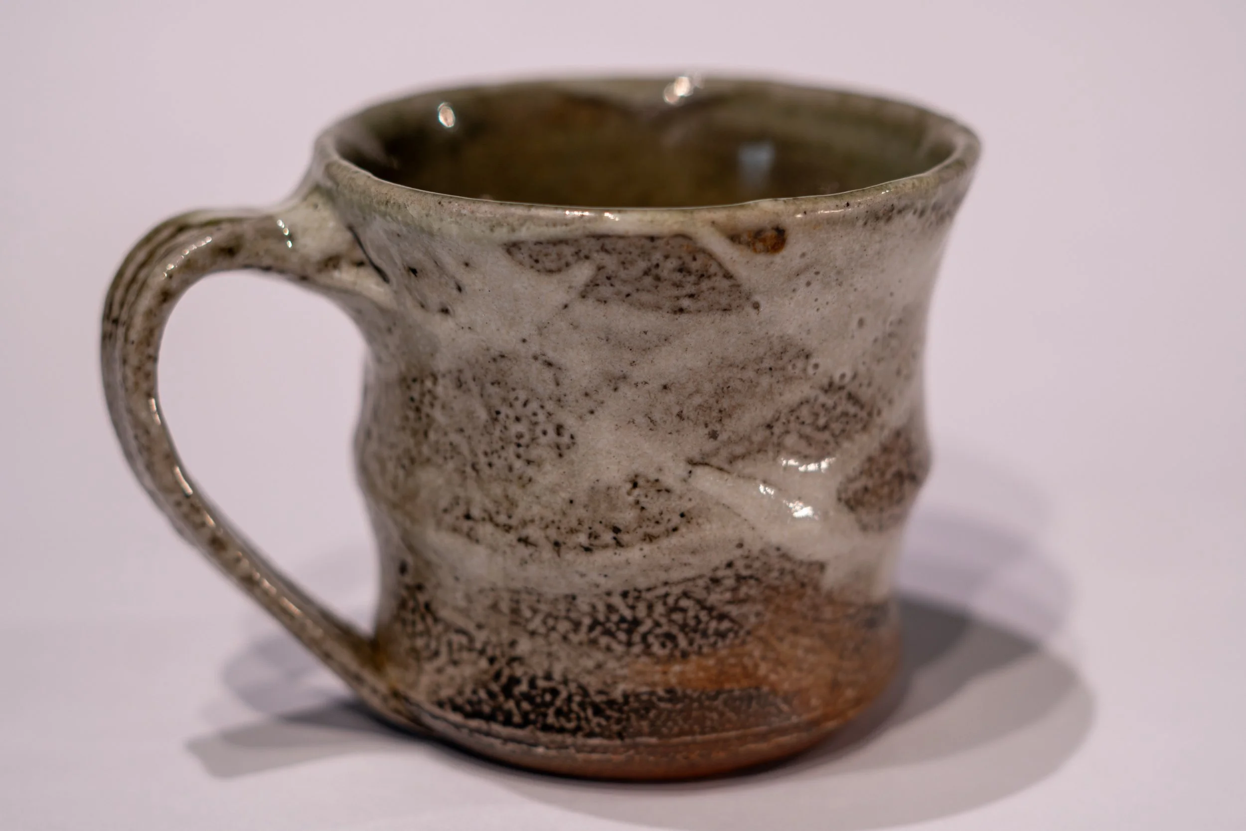 A ceramic mug with a textured, speckled glaze, featuring an artistic leaf design near the rim.