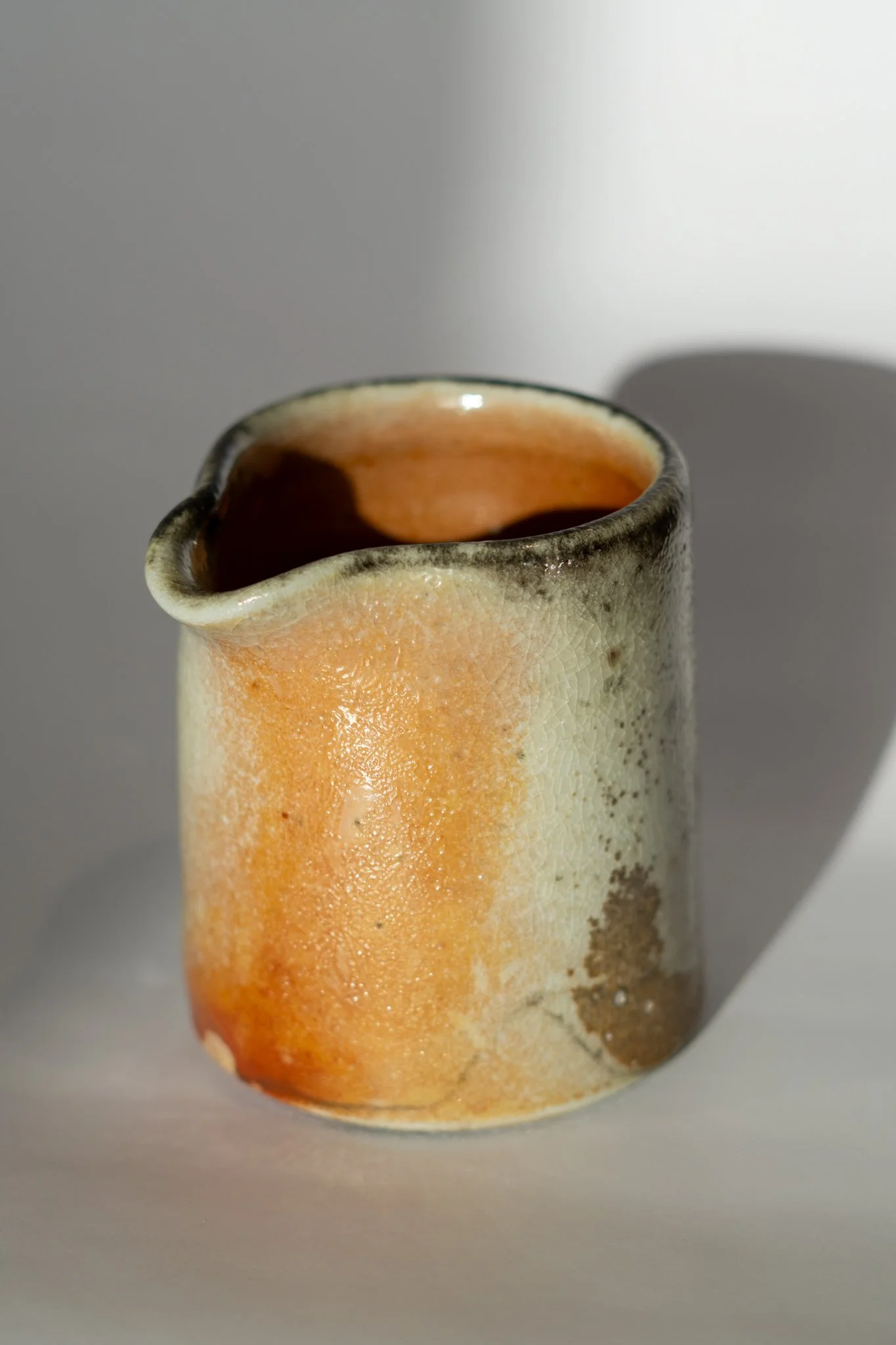 Close-up of a handmade ceramic mug with a rustic, textured glaze in shades of orange, beige, and brown, against a plain background.