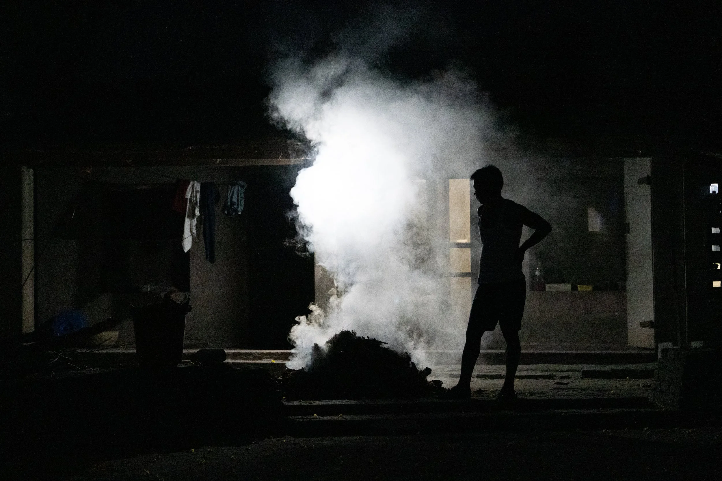 Person standing in a dark room with smoke or steam billowing from the ground and laundry hanging on a line in the background.