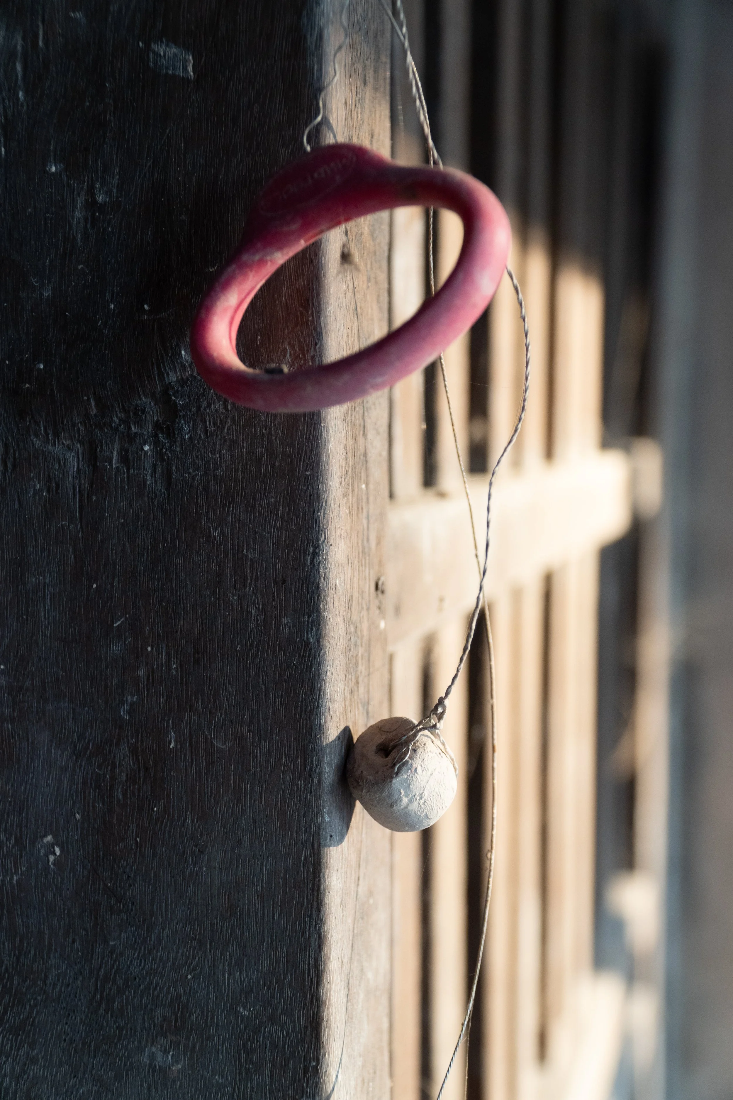 A pink boxing glove hanging on a string attached to a wooden surface with a white rock hanging beneath it, against a blurred background.