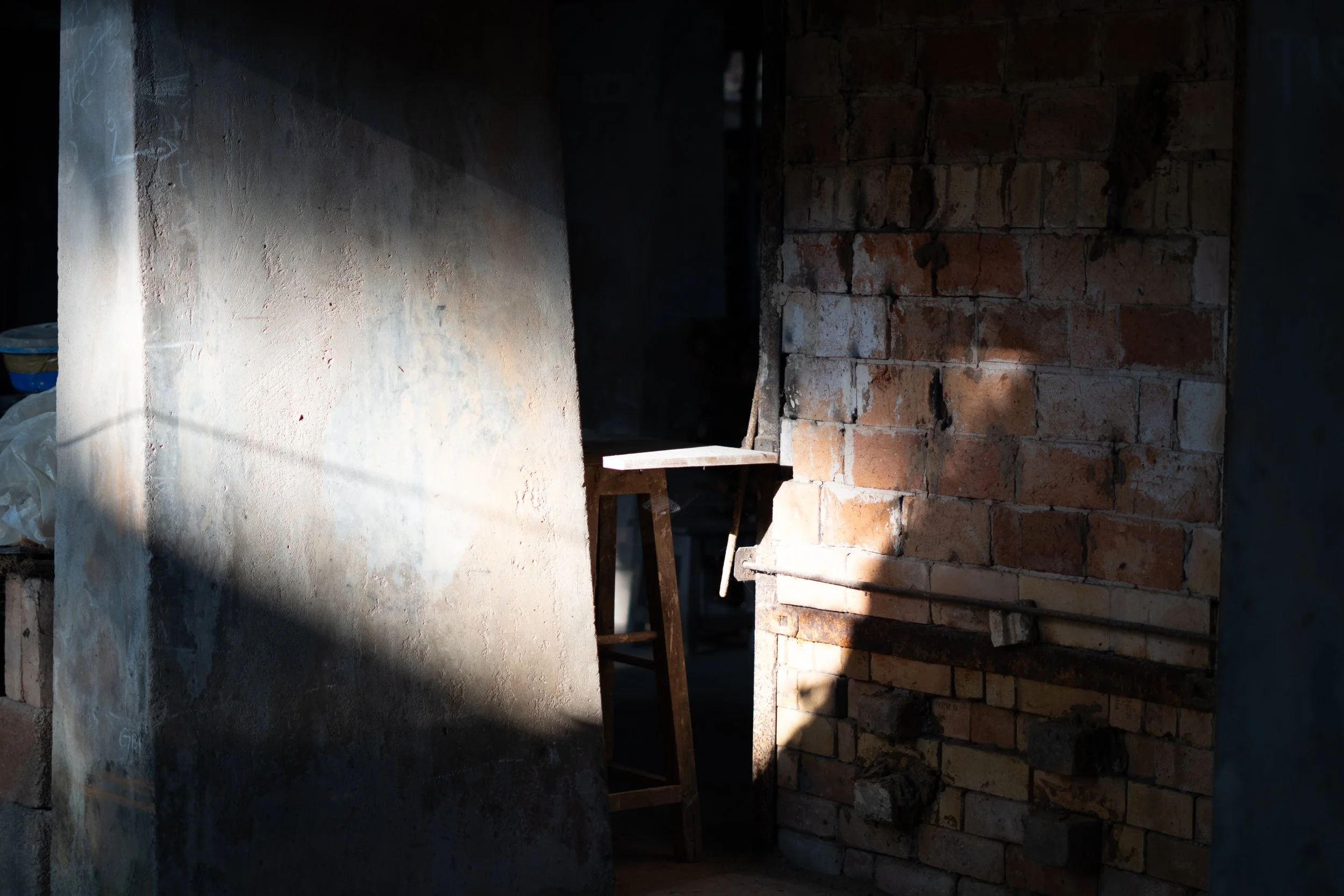 Indoor construction site with a brick wall on the right and a concrete wall on the left, with a small wooden workbench and scattered construction materials.