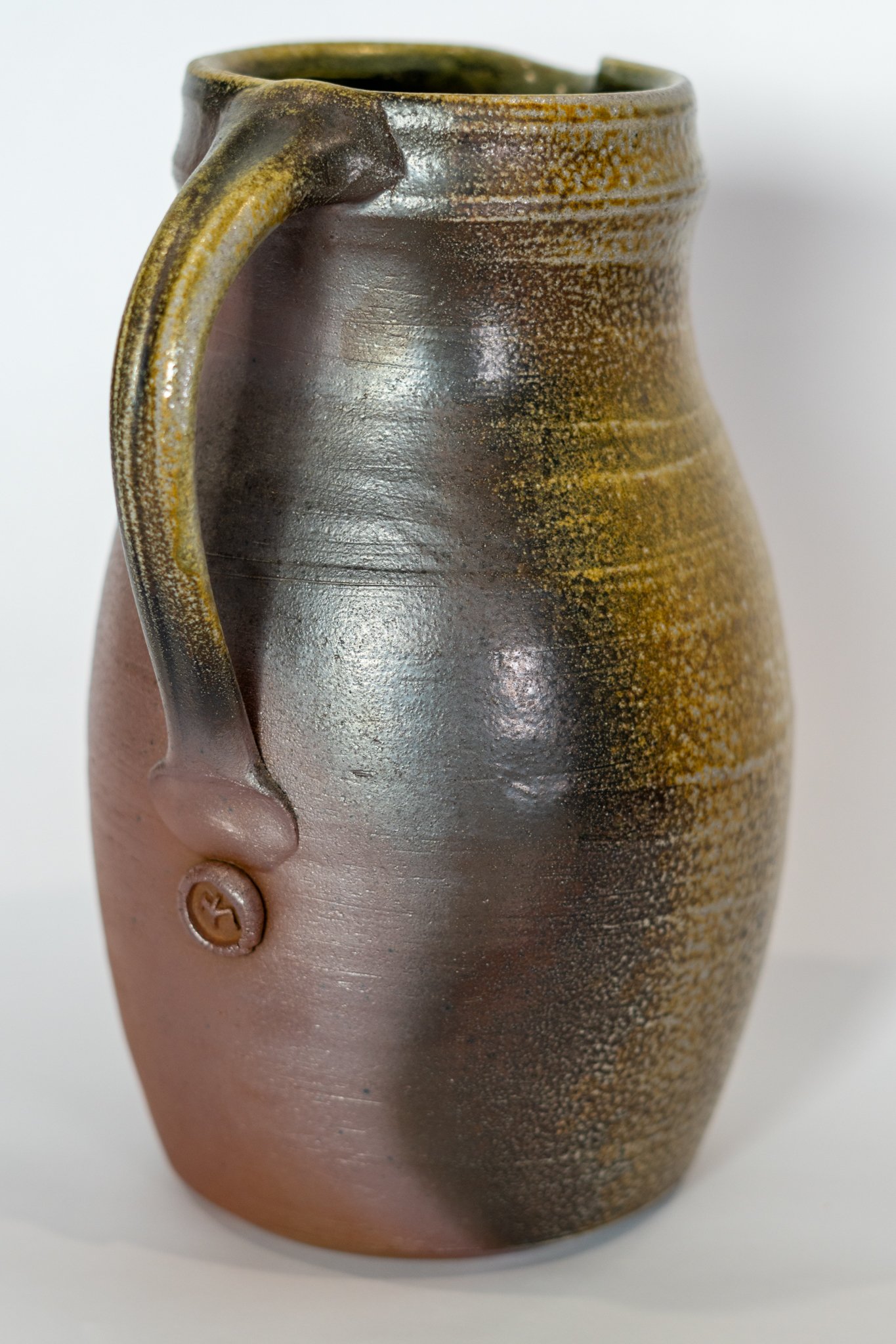 A ceramic vase with a textured, brown and yellow glaze, held by a hand with a round ring.