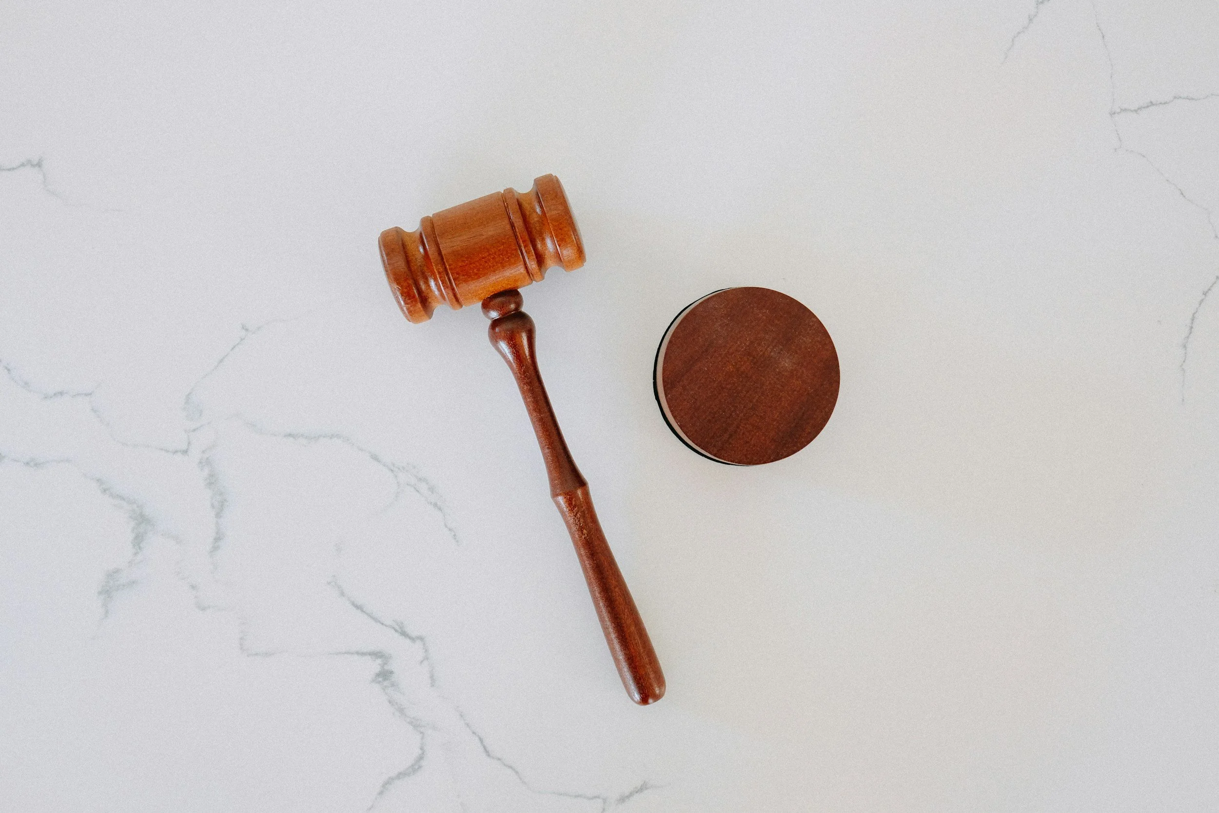 A wooden gavel resting on a white marble surface with gray veins.
