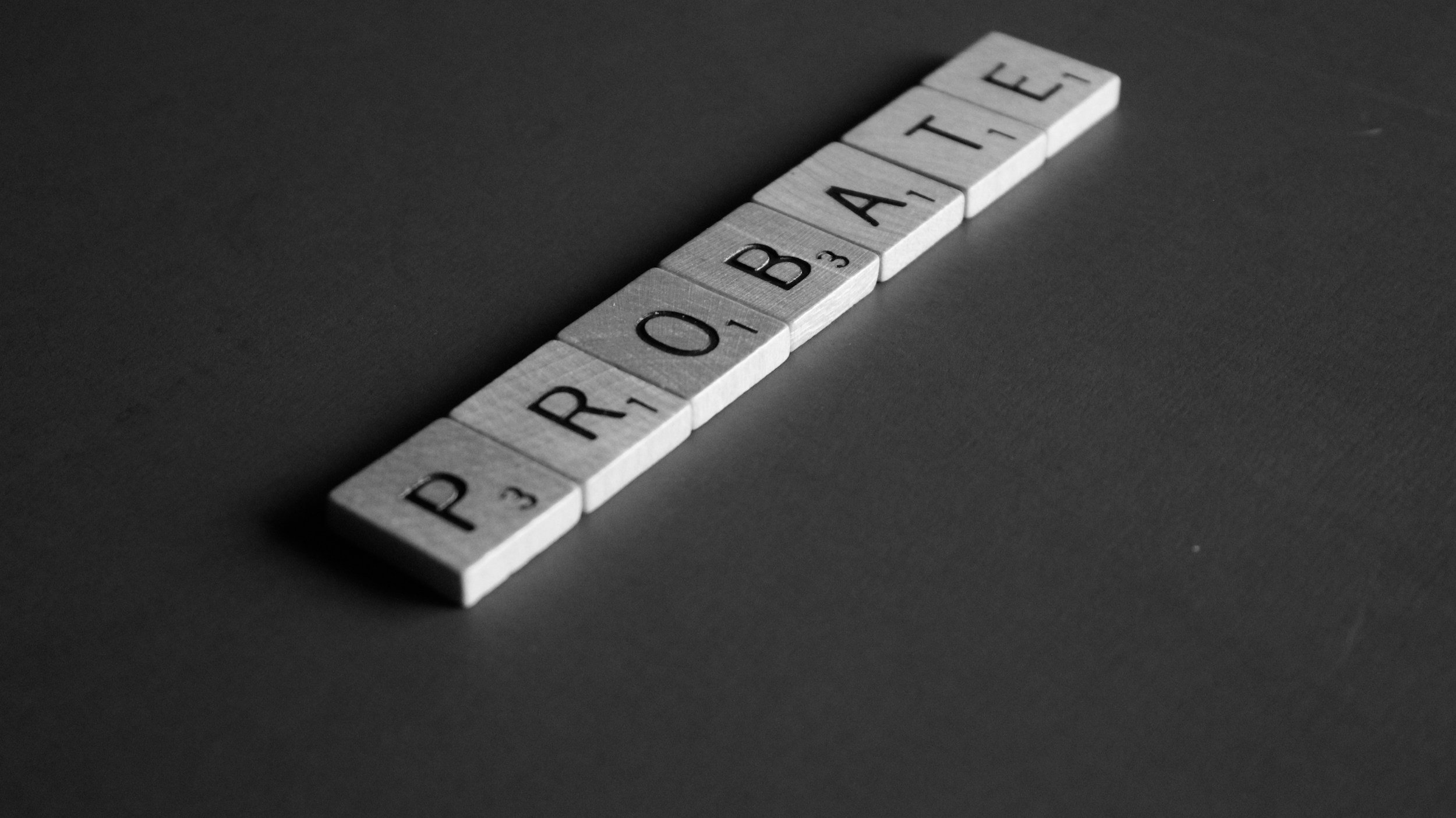 Black and white photo of Scrabble tiles spelling out the word "PRETEND" arranged diagonally on a dark surface.