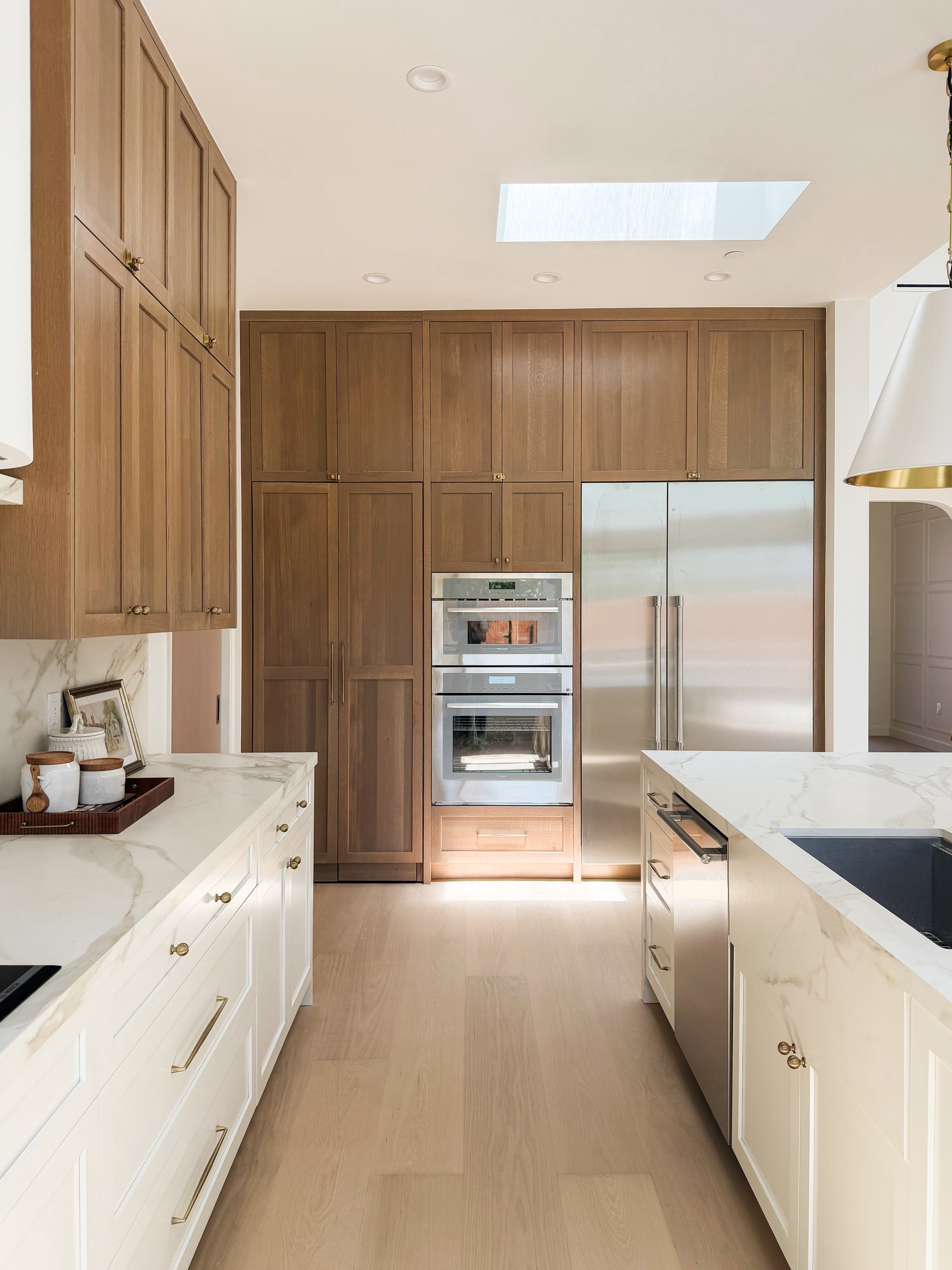 Modern kitchen with white marble countertops, wooden cabinets, stainless steel appliances, built-in oven, and a skylight on the ceiling.