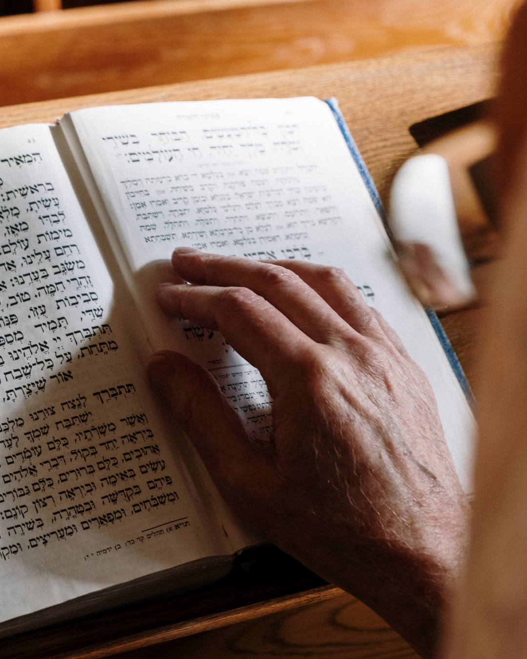 A person's hand holding a Hebrew Bible open on a wooden surface.