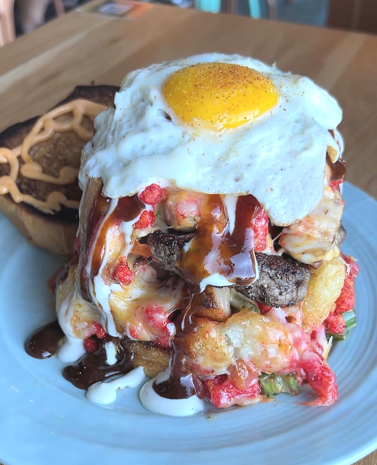 A dish with a fried egg on top, served on a bed of various ingredients including meat, sauces, and vegetables, with a side of a pastry and drizzled sauces.