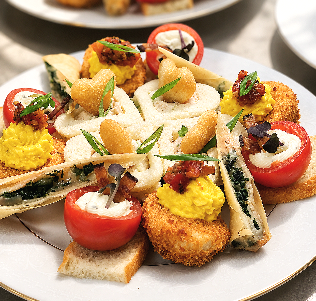 Assorted upscale appetizers on a white plate, including stuffed cherry tomatoes, mini sandwiches, breaded fried items, and egg salad with garnishes.