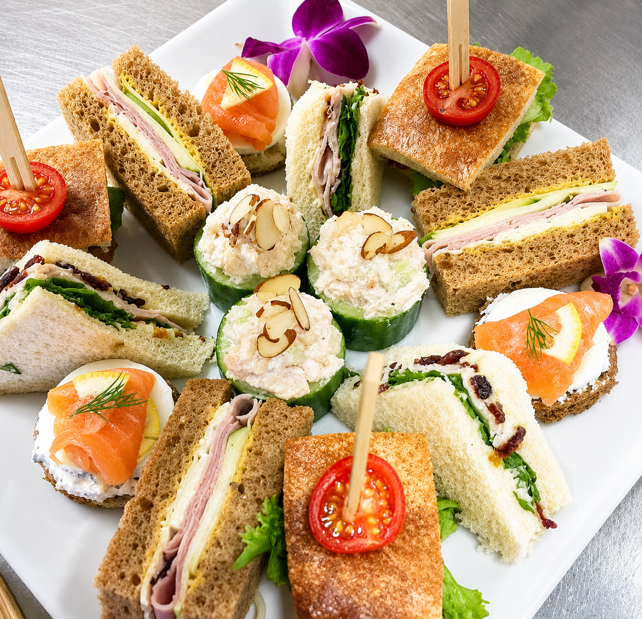 Plate of assorted finger sandwiches with various fillings, garnished with cherry tomatoes, lemon slices, and purple orchids.