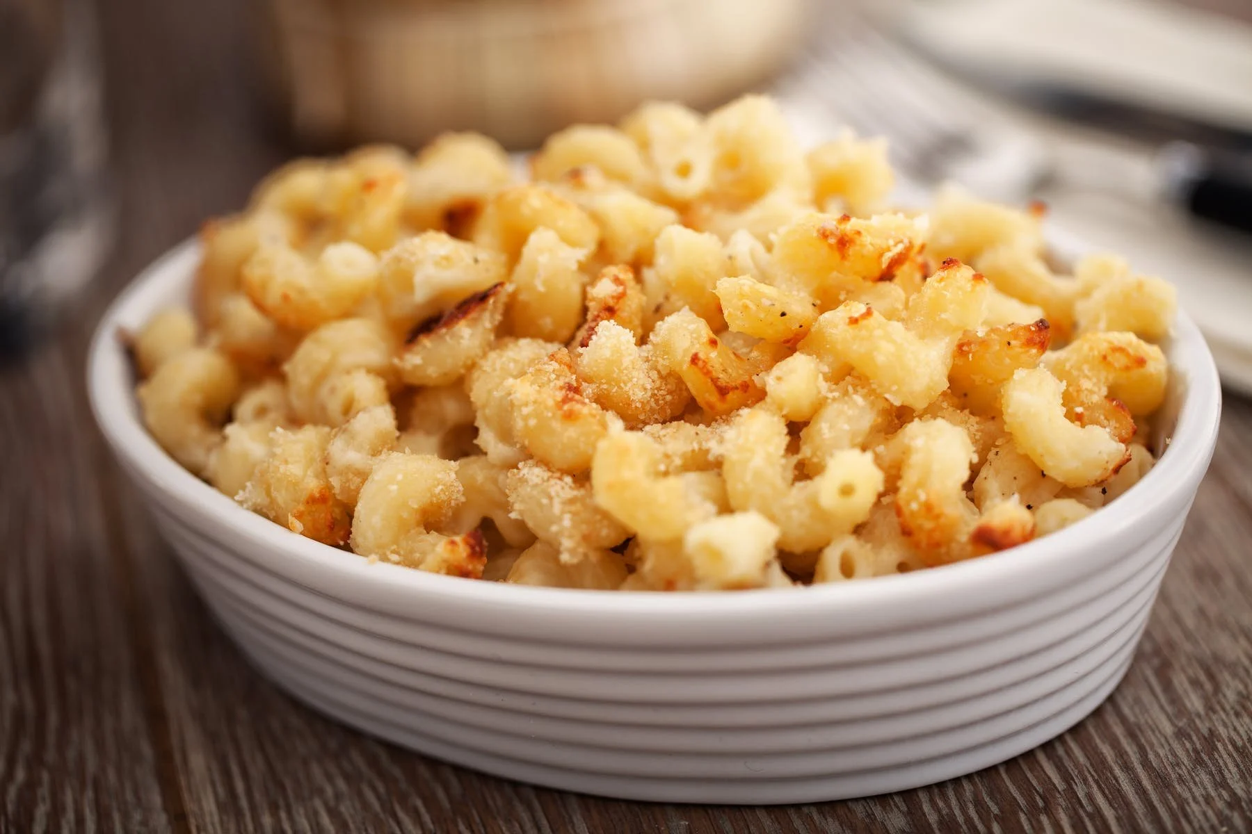 Bowl of cooked macaroni and cheese with a breadcrumb topping on a wooden surface.