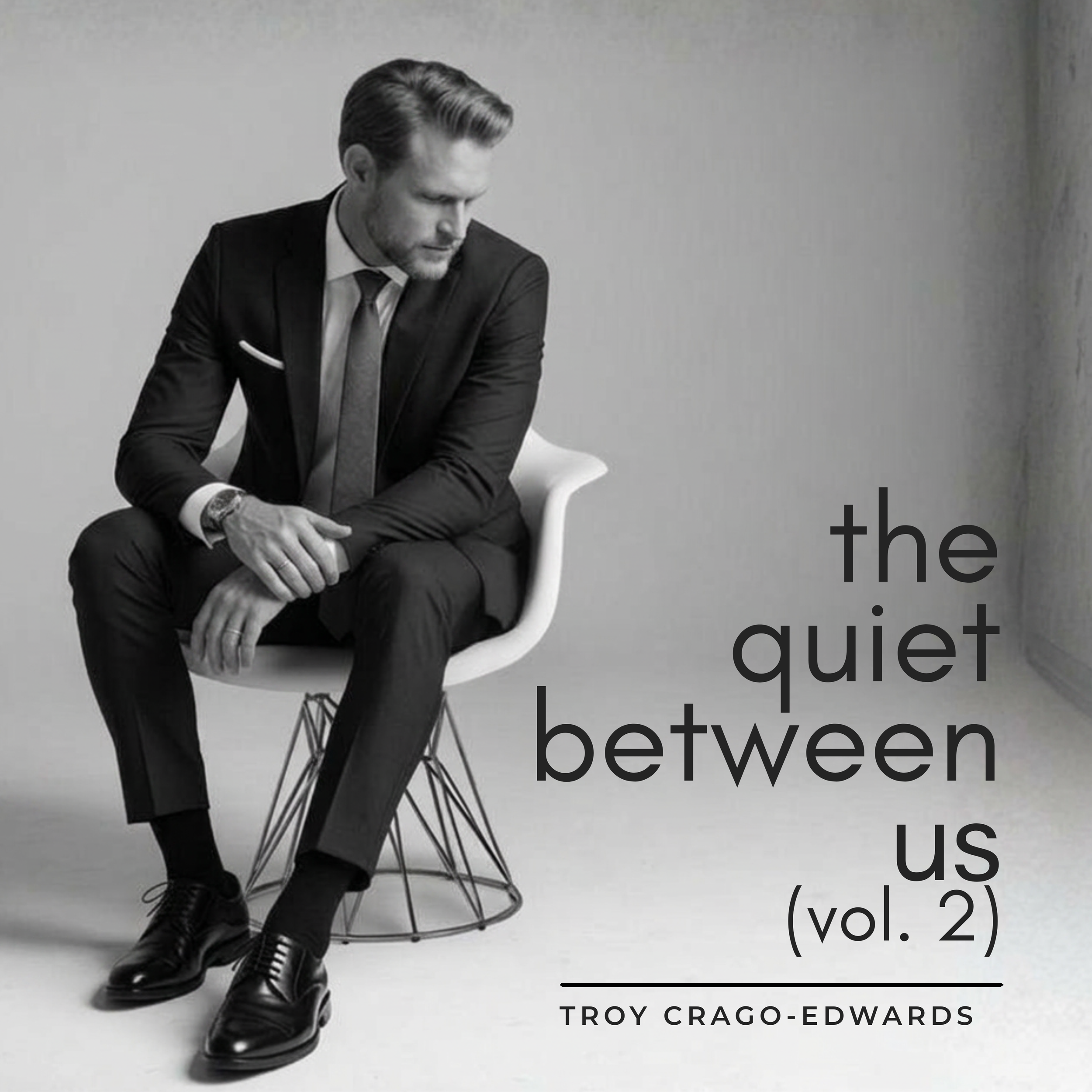 A black-and-white photograph of a man in a suit sitting on a modern chair against a plain wall. The image features overlaid text that reads 'The quiet between us vol. 2' and 'TROY CRAGO-EDWARDS'.