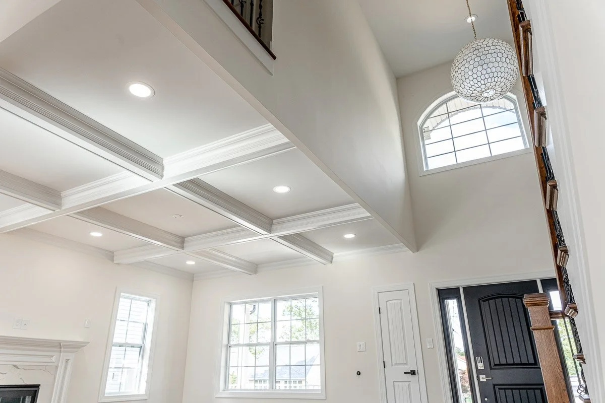 Interior of a modern home with white walls, large windows, a staircase, and a ceiling with recessed lighting and decorative molding.
