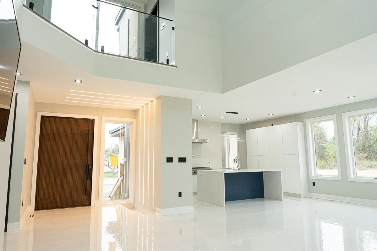Modern, spacious, white kitchen and living area with large windows and an entry door.
