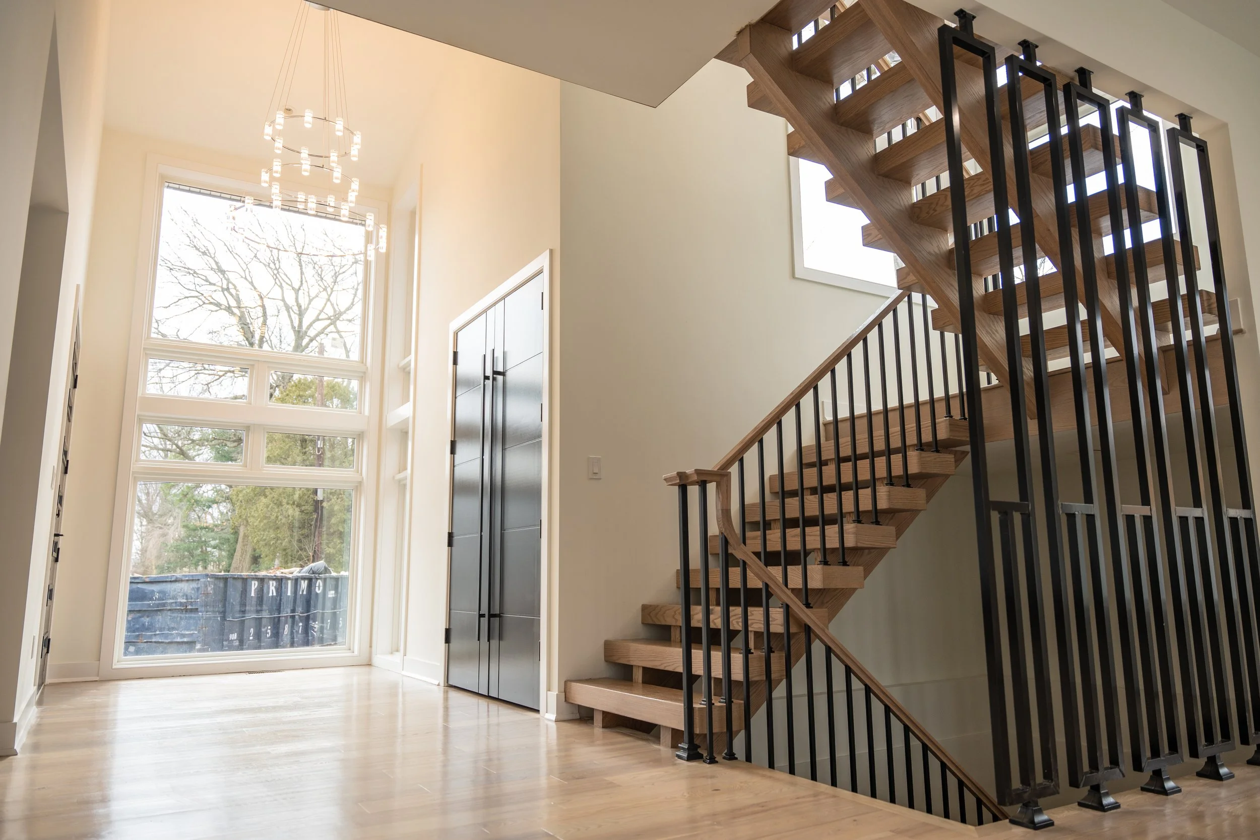 Interior view of a modern house with a staircase, large window, and minimal decor.