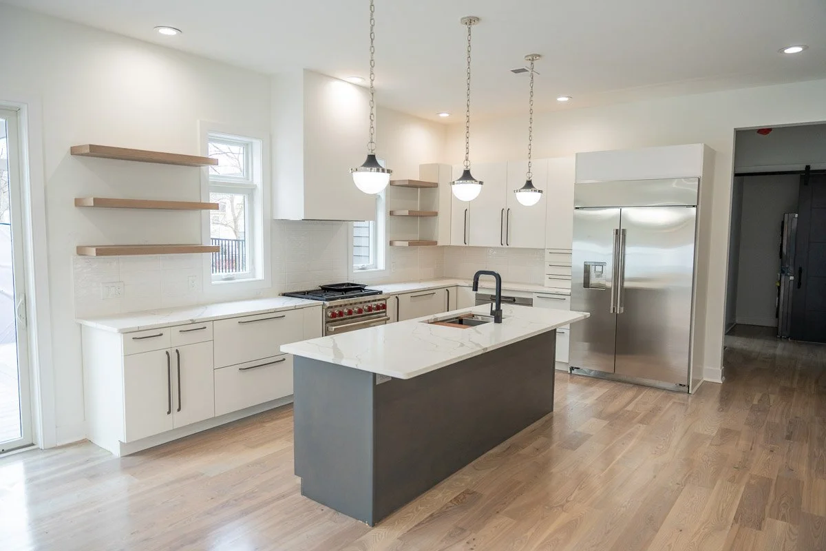 Modern kitchen with white cabinets, a black island with a white marble countertop, stainless steel refrigerator, and open wooden shelves. There are three pendant lights hanging above the island.