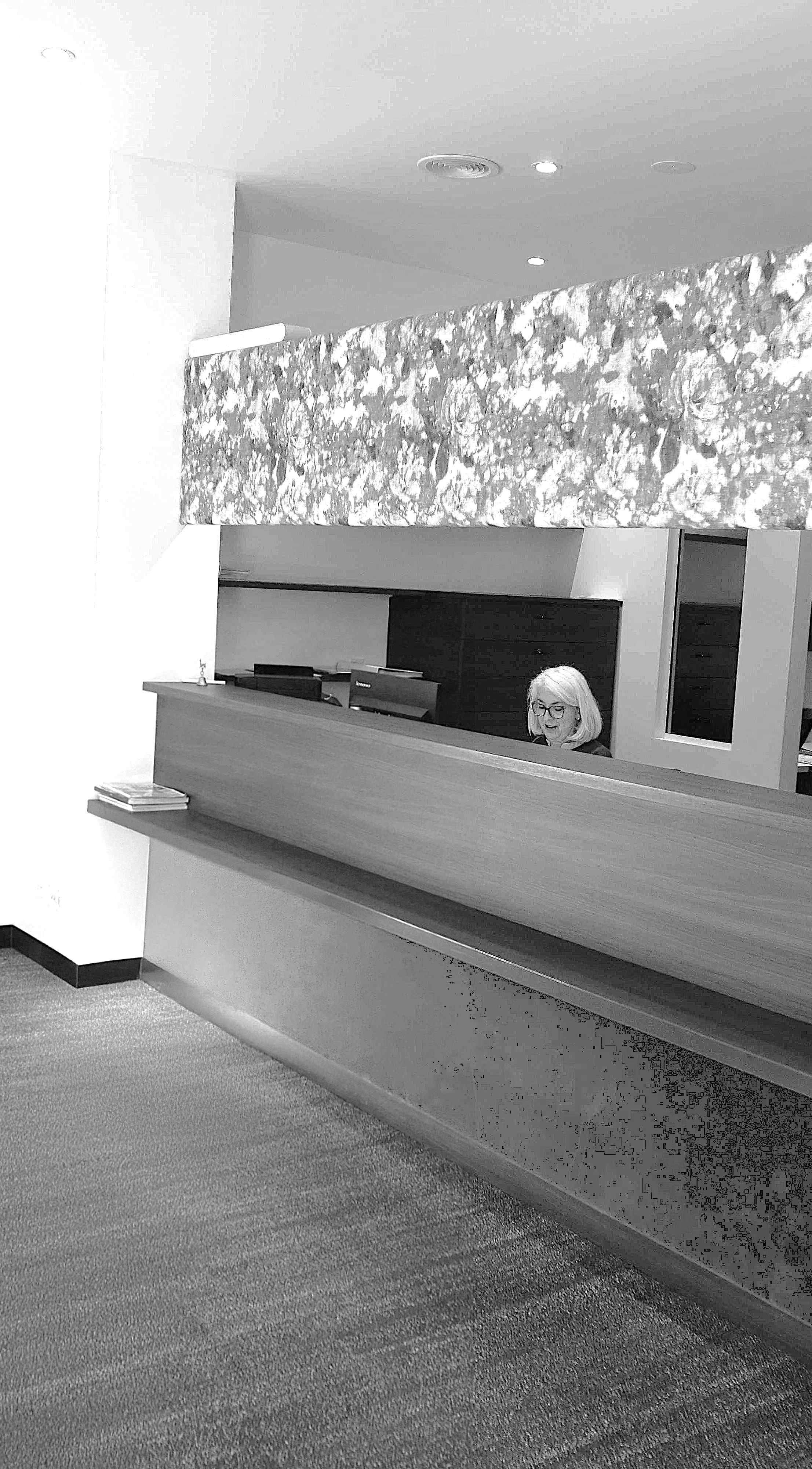 A woman with glasses smiling behind a reception desk in an office.
