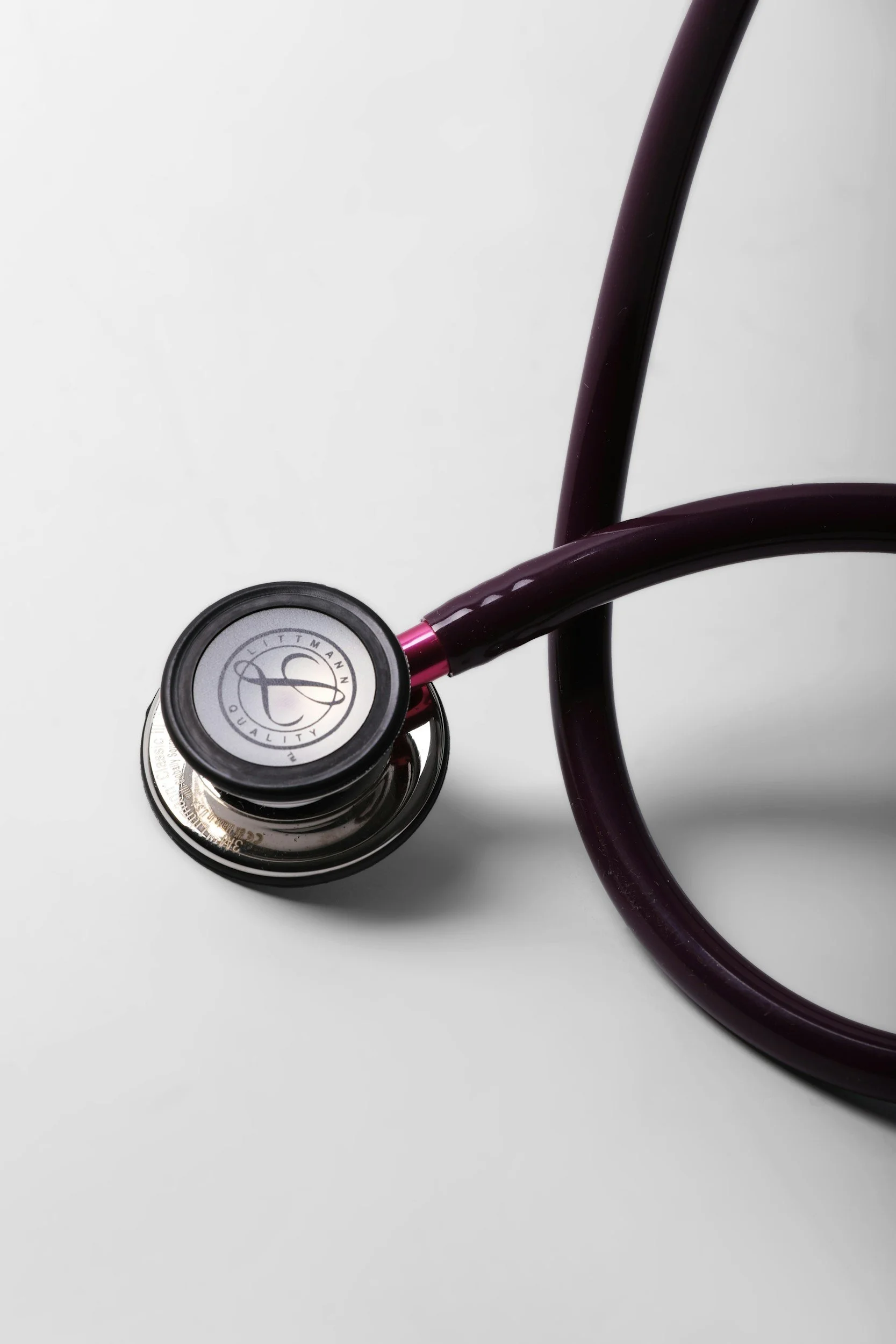 Close-up of a stethoscope on a white surface, showing the chest piece with a logo and part of the flexible tubing.