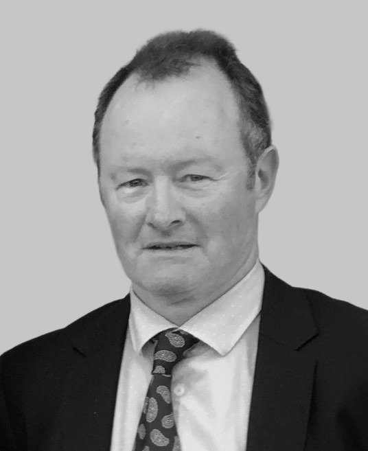 A middle-aged man in a suit and tie posing for a portrait against a plain background.