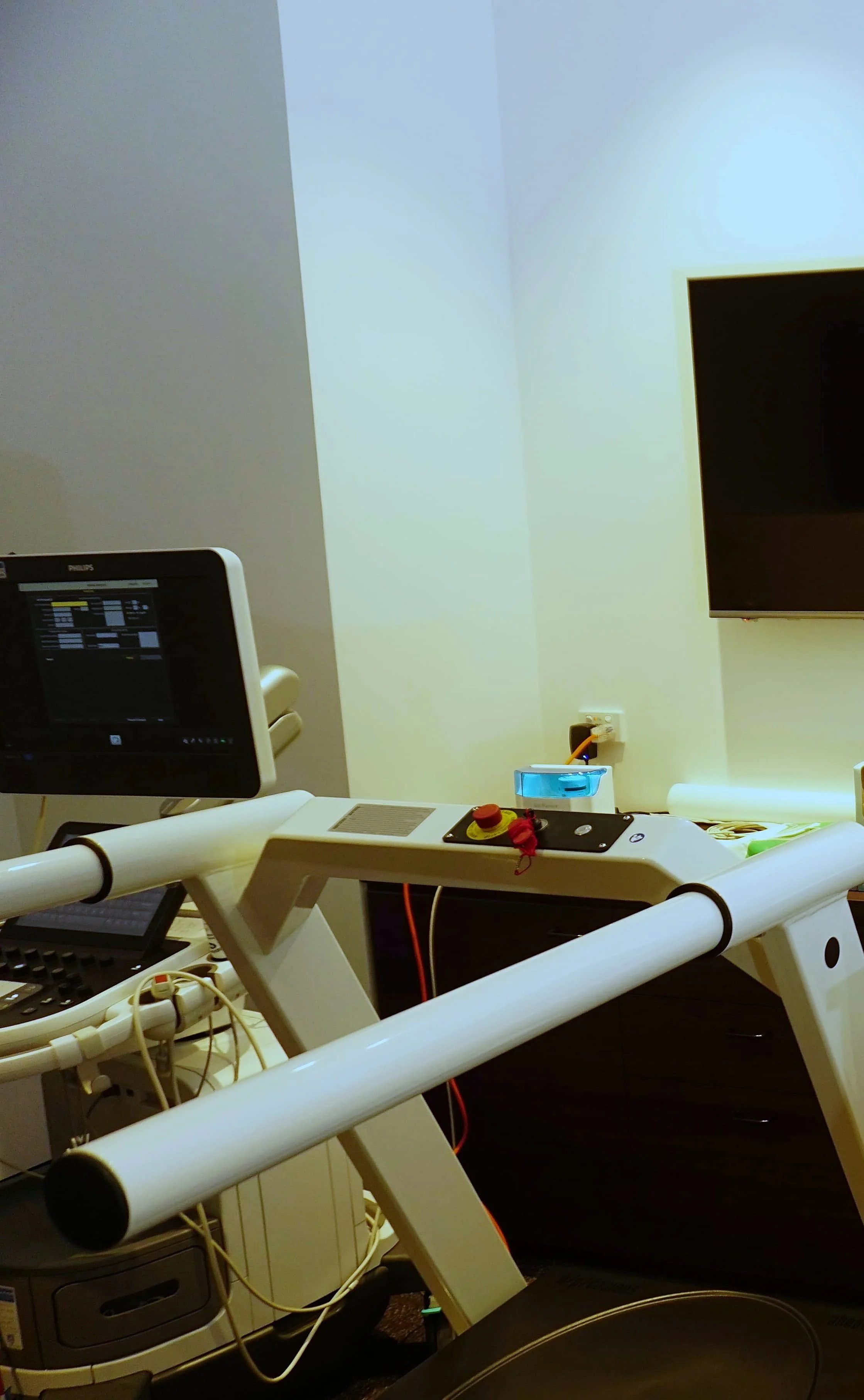 Hospital room with medical equipment, including a monitor, a control panel with buttons, and a flat-screen TV on the wall.