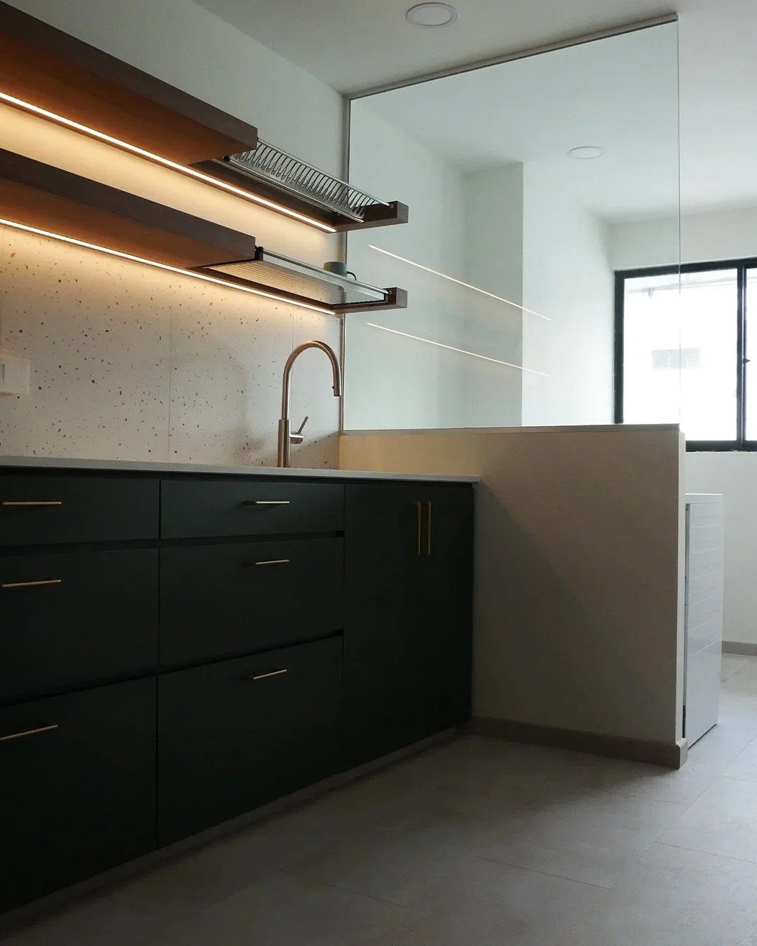 Modern kitchen with black cabinets, a sink with a faucet, open shelves with lighting, a light-colored speckled tile backsplash, and a window letting in natural light.