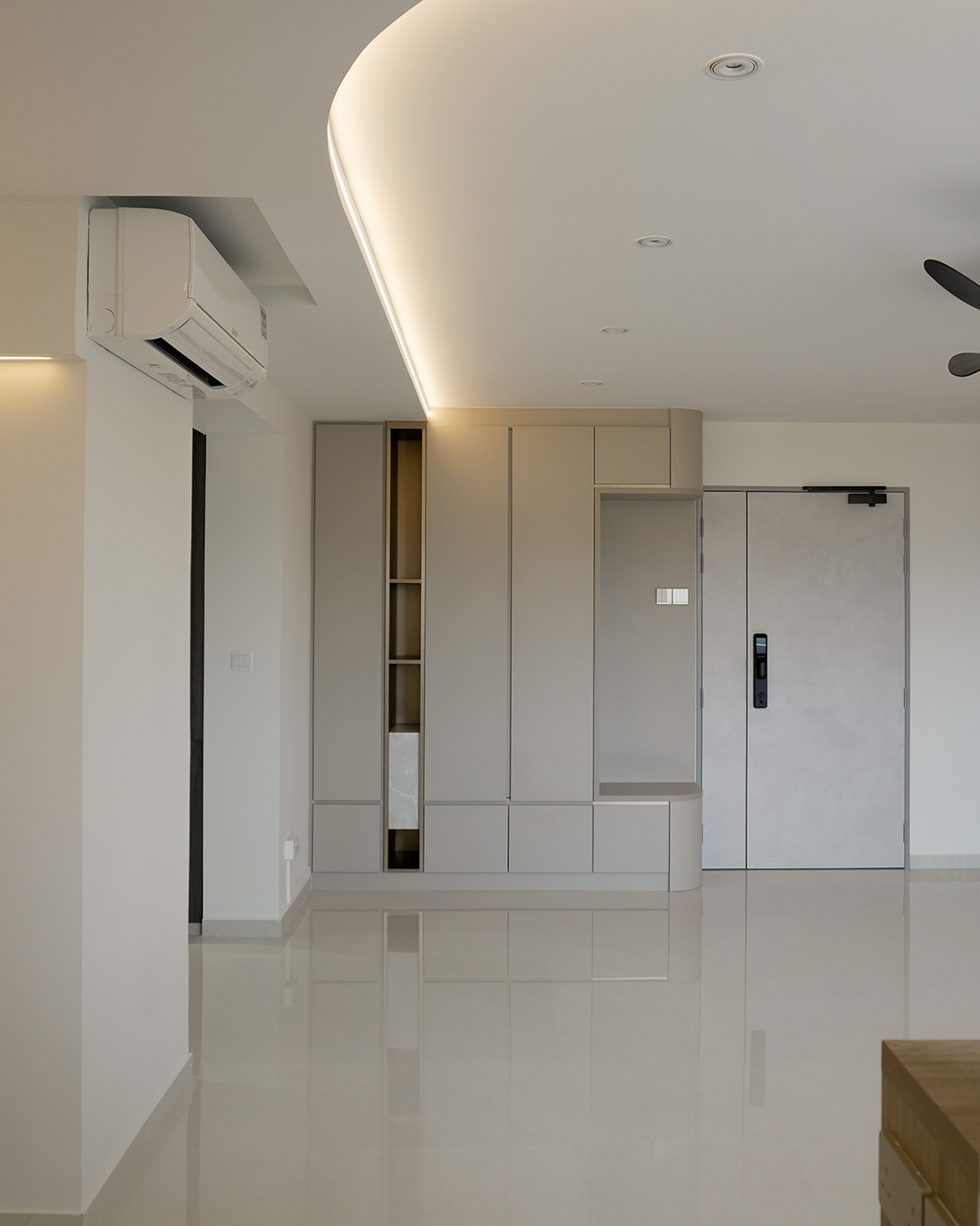 Minimalist interior living space with beige built-in cabinets, a door, a wall-mounted air conditioner, and a ceiling fan.
