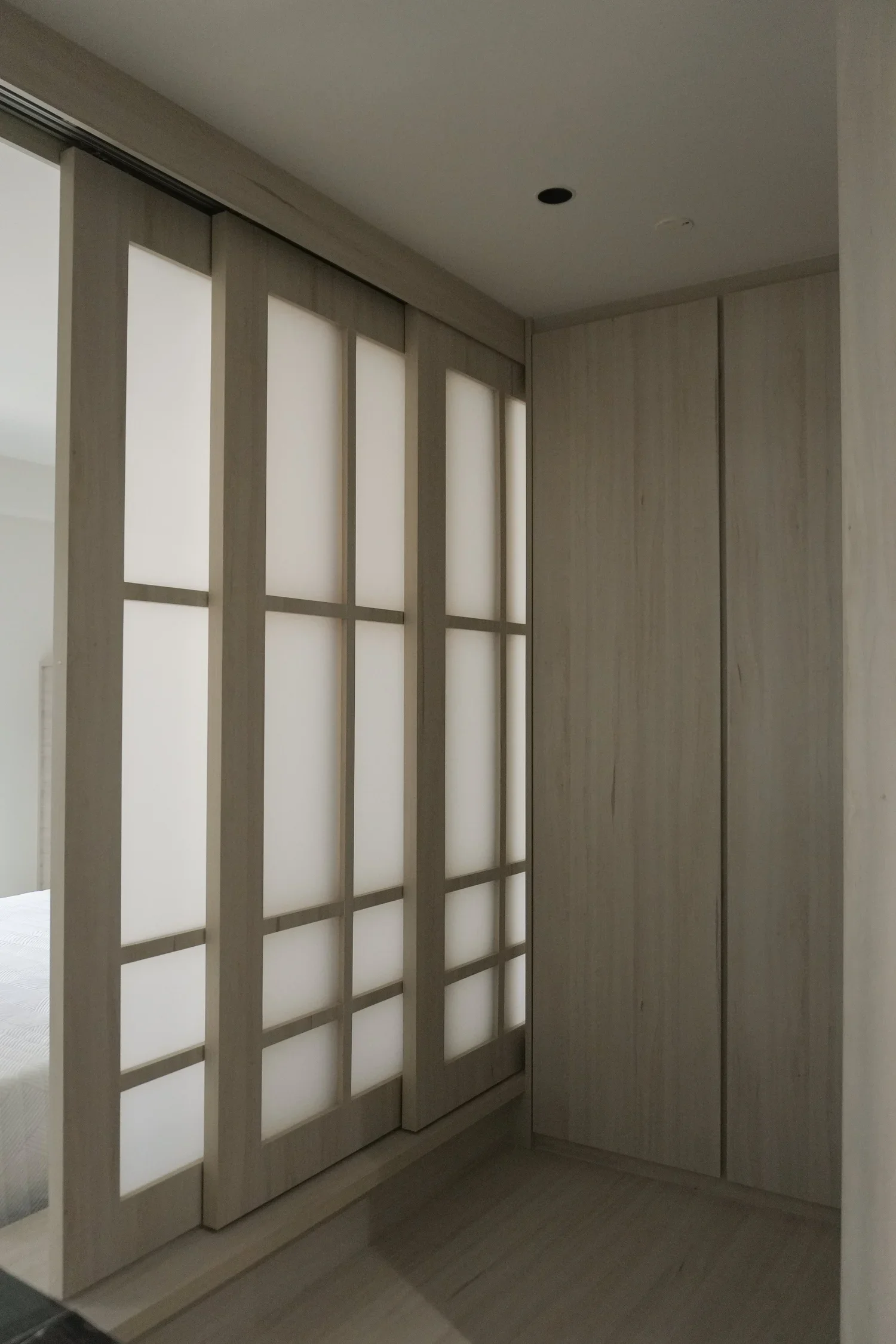 Interior view of a room with frosted glass sliding doors and light wood paneling on the wall.