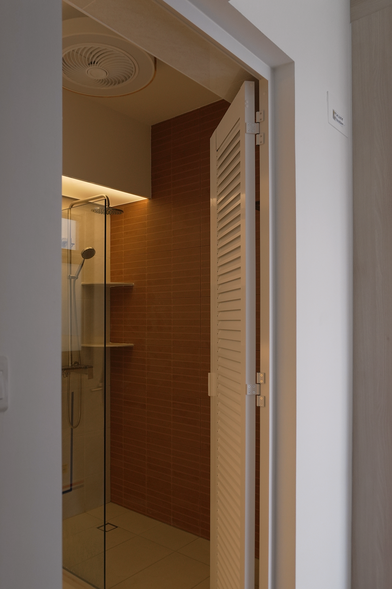 View of a modern shower area with glass door, showerhead, and brown tiled wall inside a bathroom.