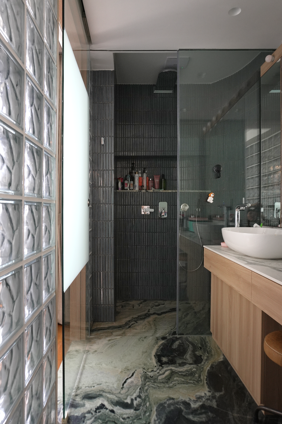 Modern bathroom with a glass shower enclosure, black tiled walls, a wooden vanity with a marble countertop, and a white vessel sink.