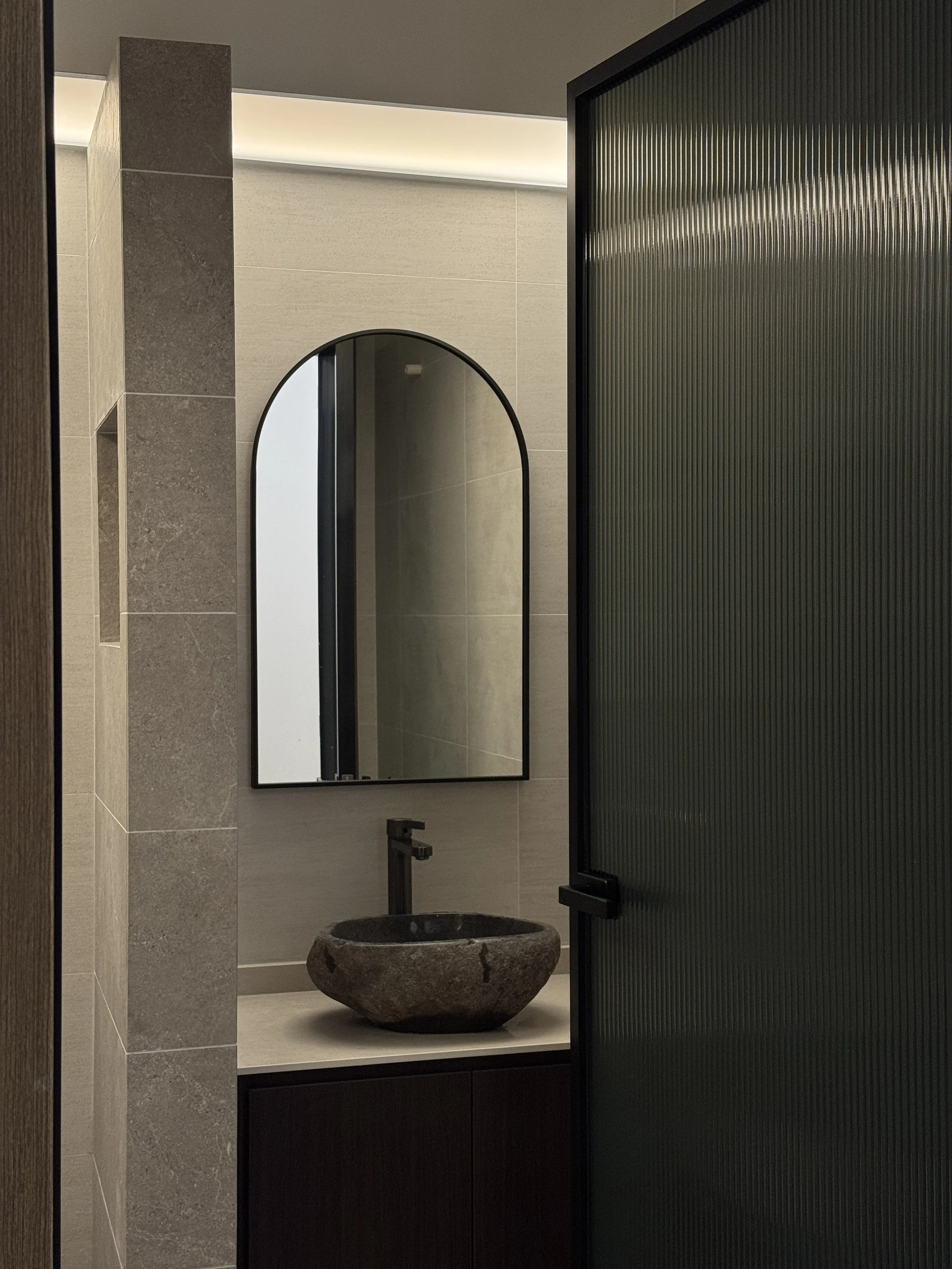 Modern bathroom with a stone vessel sink, a circular mirror, and textured glass partition.