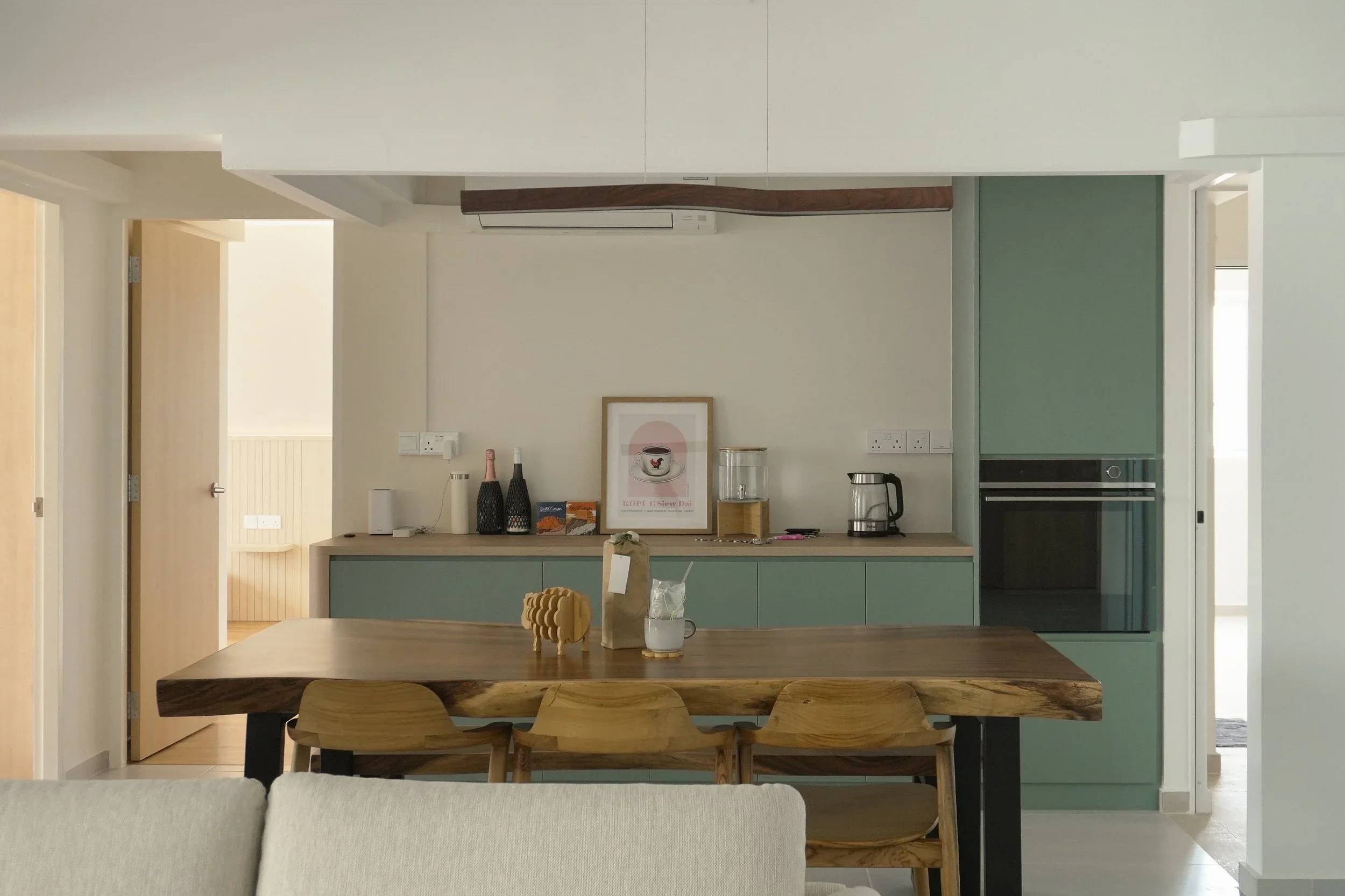 Interior view of a modern kitchen and dining area with a wooden table and chairs, a mint green cabinet, and various decorative items and appliances on the counter.