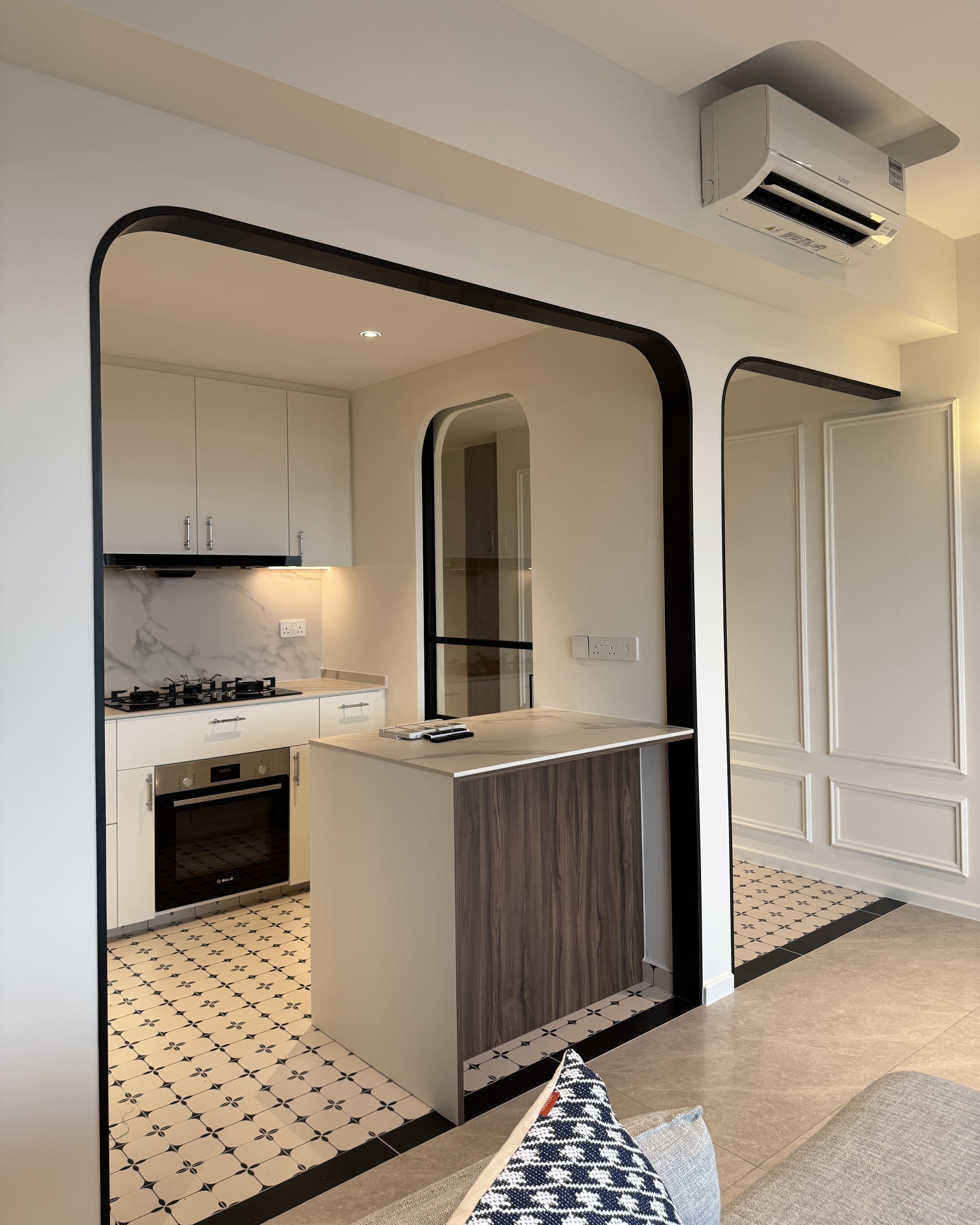 Modern kitchen with white cabinets, a marble backsplash, and a built-in oven. Black and white patterned floor tiles and a black-framed doorway.