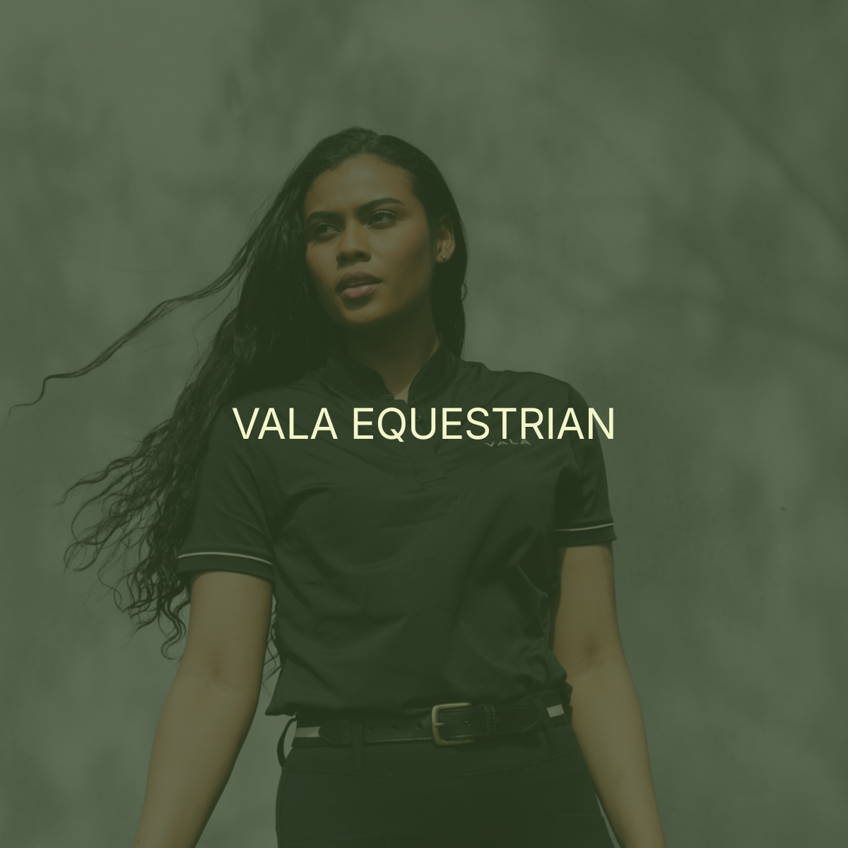 A woman with long black hair wearing a black equestrian uniform standing outdoors with trees in the background, with the overlay text "VALA EQUESTRIAN".