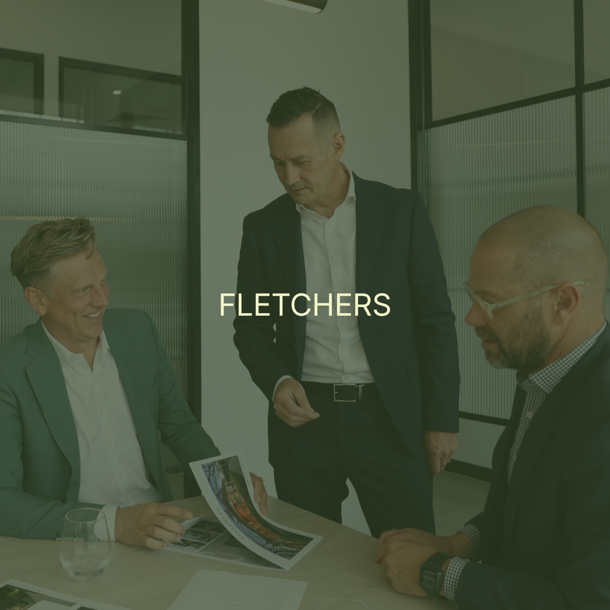 Three men in business attire having a discussion in an office conference room, with one man showing a printed document to the others.